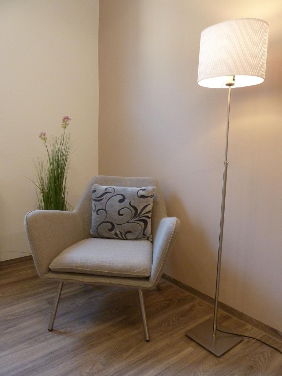 Ein Sessel mit Kissen, eine Stehlampe und eine Pflanze in einem Raum mit Holzboden.