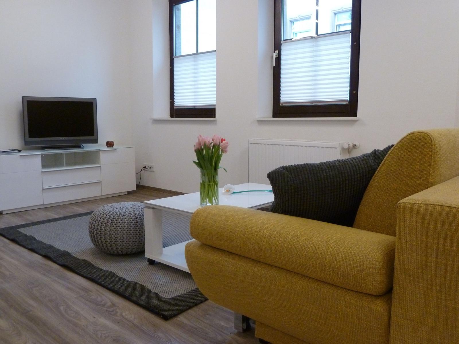 Wohnzimmer mit gelbem Sofa, weißem Couchtisch und Fernseher auf Schrank.