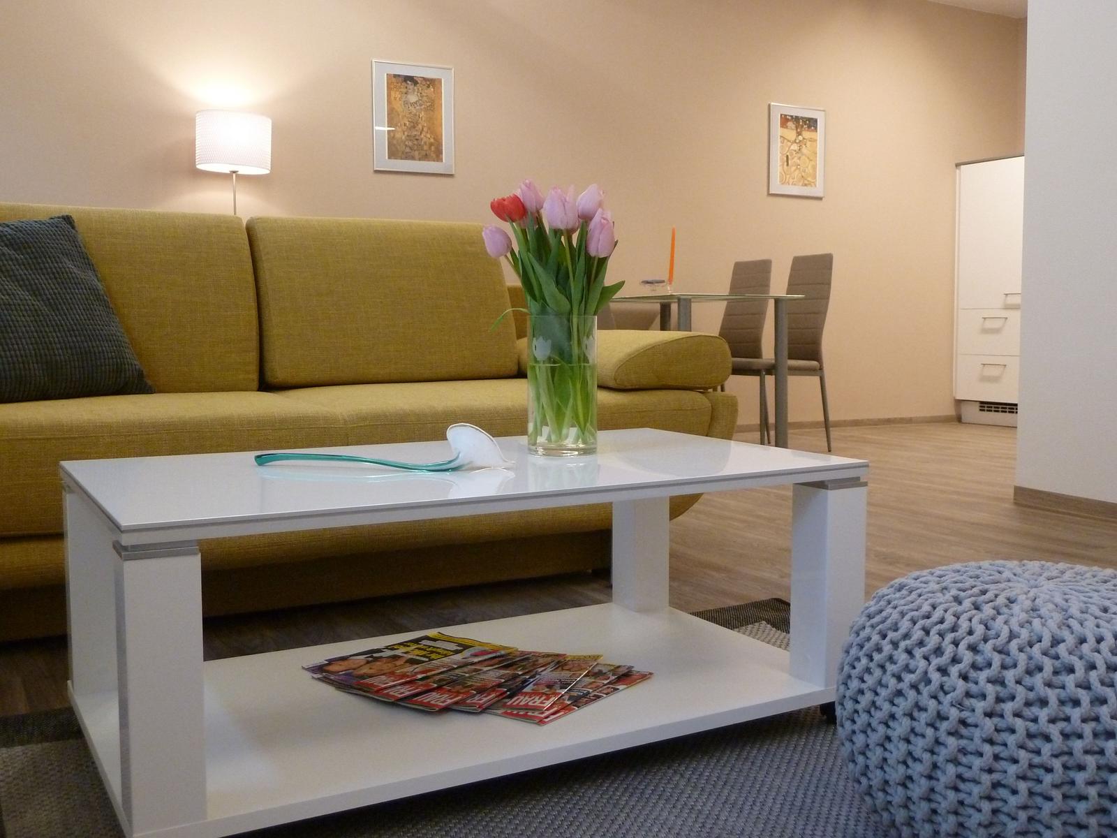 Wohnzimmer mit gelbem Sofa, weißem Couchtisch und Blumen.