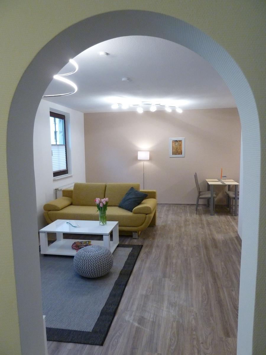Wohnzimmer mit gelbem Sofa, Tisch und Stühlen. Durchgang mit Bogen.