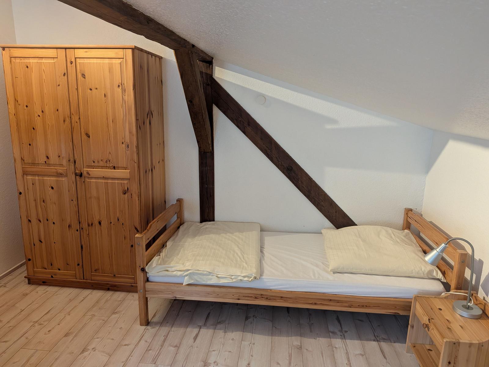 Schlafzimmer mit Holzbett, Kleiderschrank und Nachttisch unter Dachschrägen.
