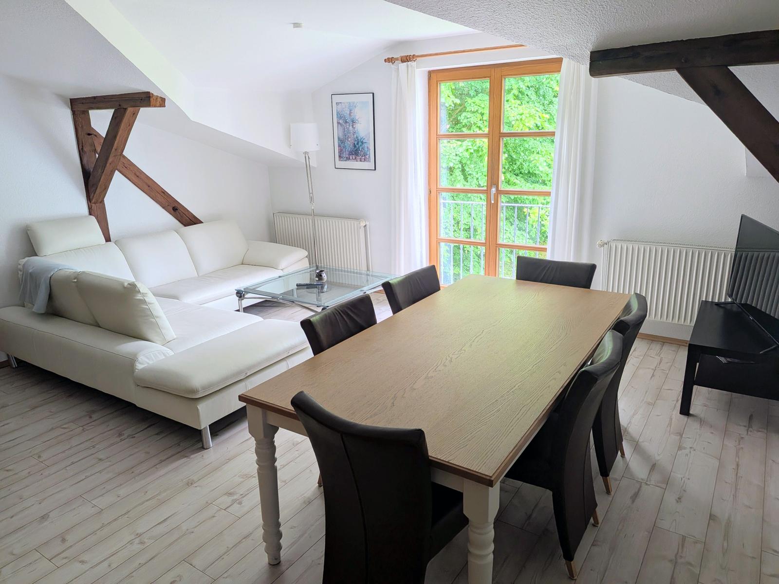 Wohn- und Essbereich mit Sofa, Esstisch und Fenster zum Balkon.