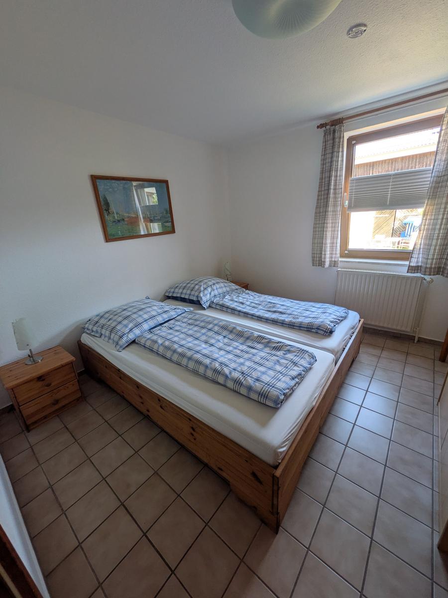 Zimmer mit zwei Einzelbetten, Holzkommode und Fenster mit Jalousie.