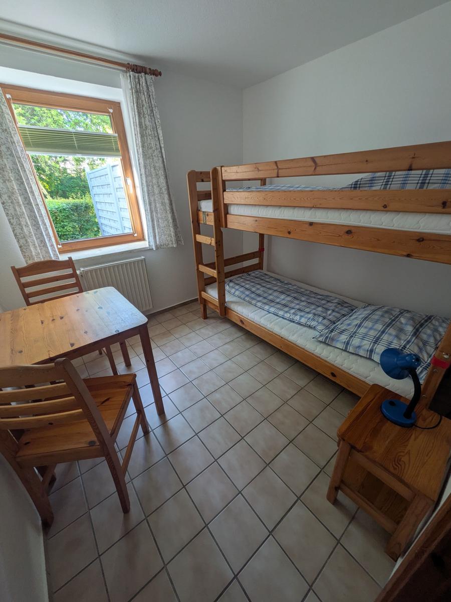 Zimmer mit Doppelstockbett, Holztisch und Stühlen, Fenster mit Blick auf Garten.