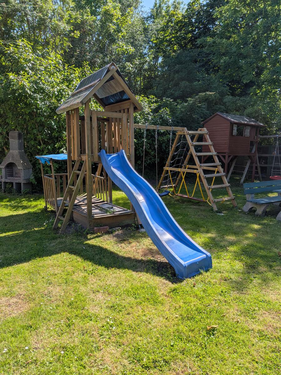 Hinterhof mit Spielplatz, Rutsche und Schaukel. Grasfläche und Bäume im Hintergrund.