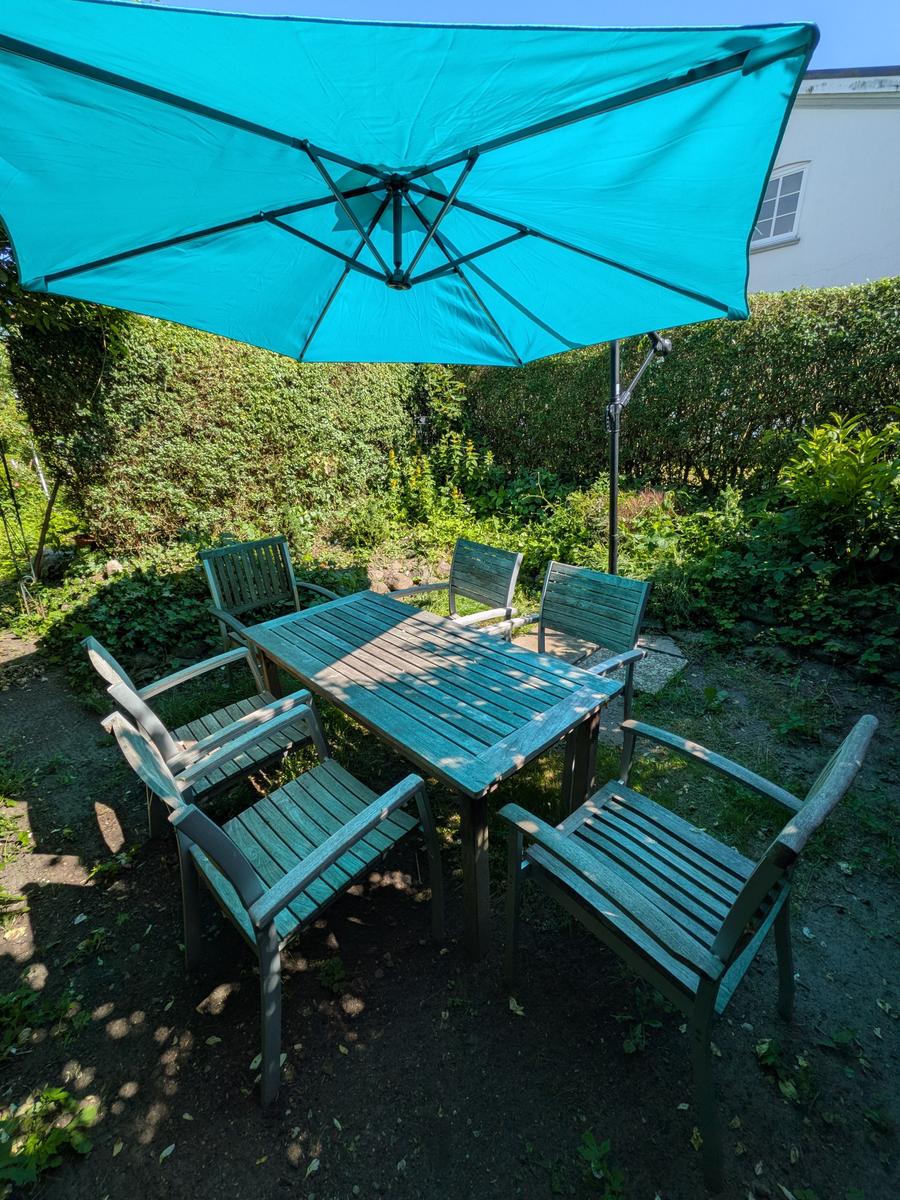Garten mit Holztisch, sechs Stühlen und blauem Sonnenschirm.