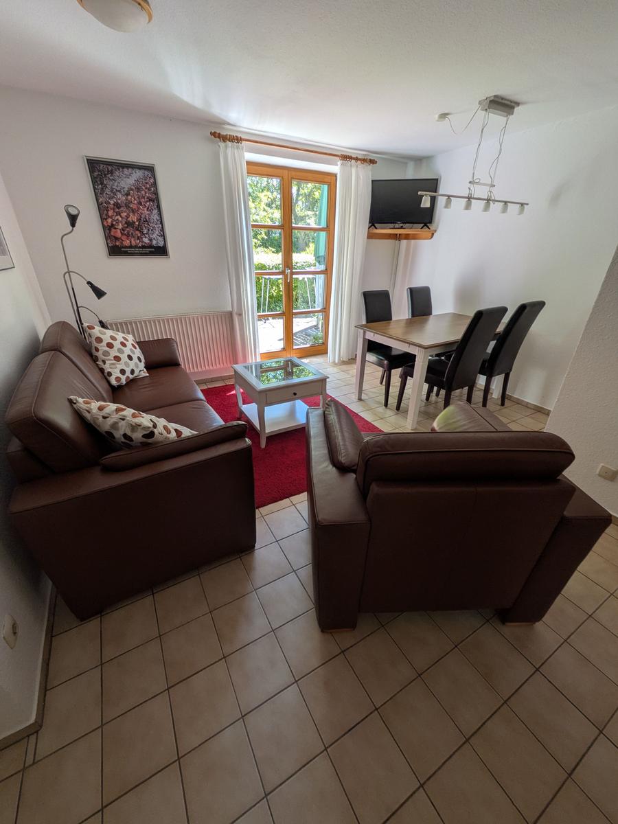 Wohn- und Essbereich mit Sofa, Sessel, Esstisch und TV. Terrasse mit Blick auf Grün.