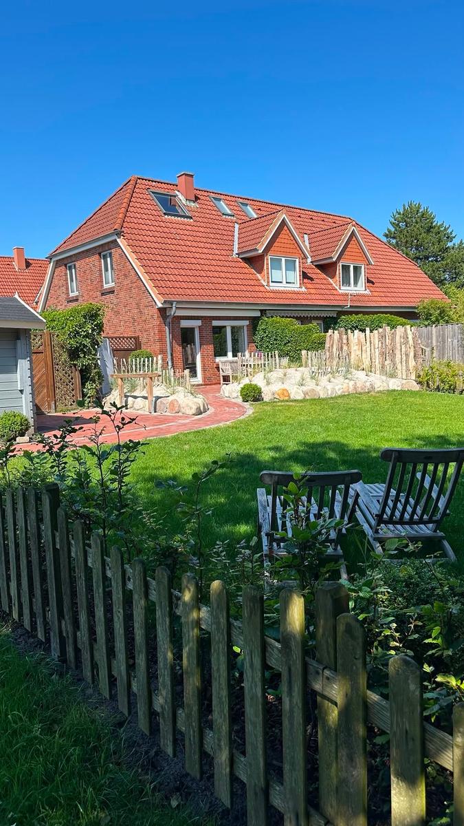 Ein zweistöckiges Haus mit rotem Dach und Garten mit Holzgeländer.