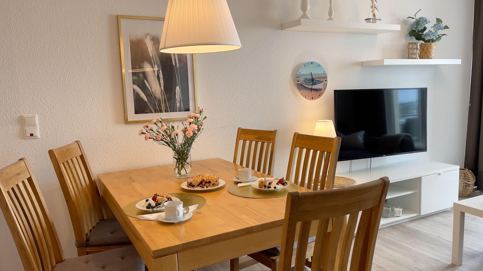 Esstisch mit vier Stühlen, Fernseher und Wanduhr im Wohnbereich.
