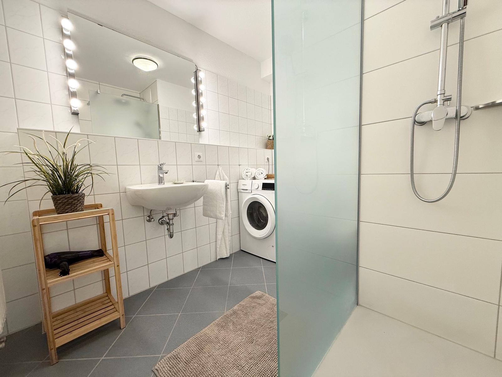 Badezimmer mit Dusche, Waschmaschine und Spiegel mit Lichterkette.