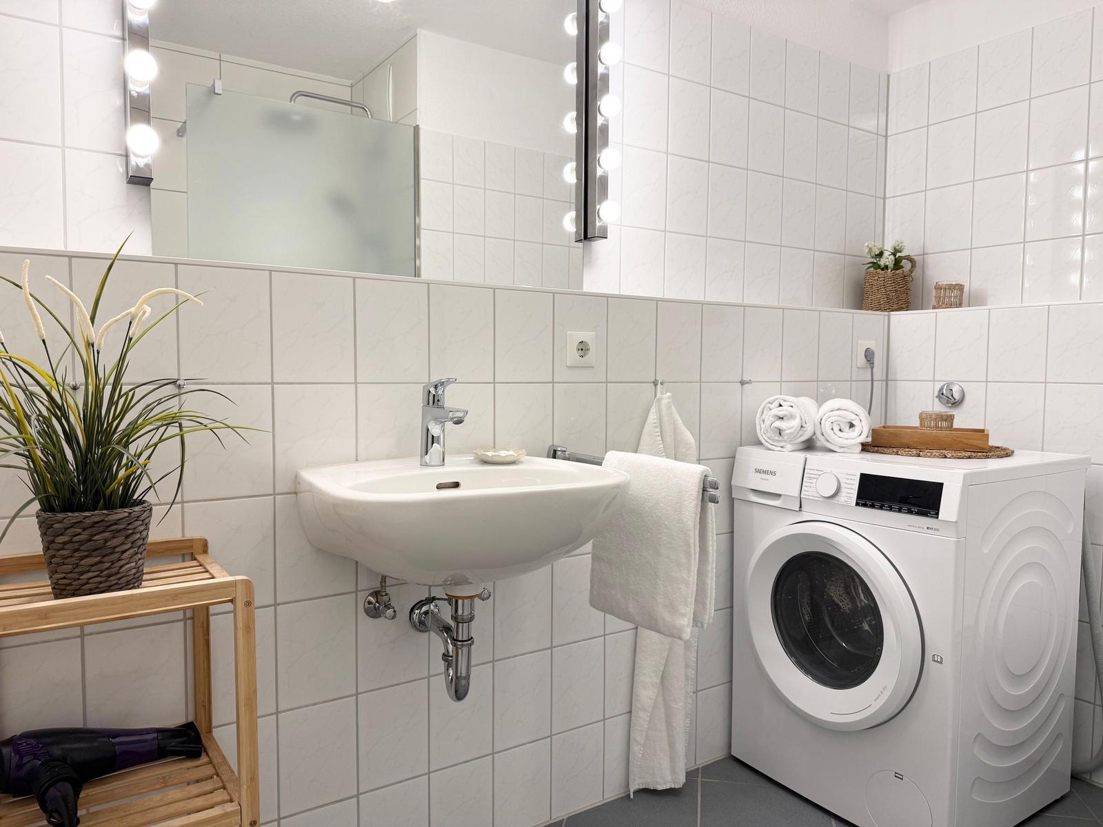 Badezimmer mit Waschmaschine, Spiegel und Pflanze.