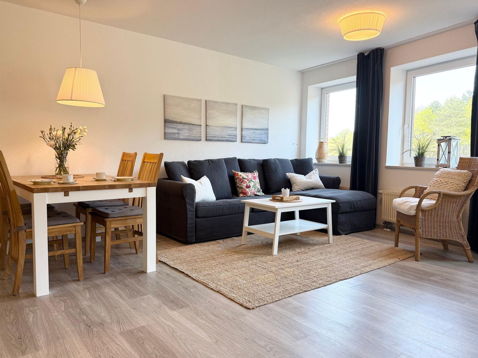 Wohn- und Essbereich mit Sofa, Esstisch und Fenstern.