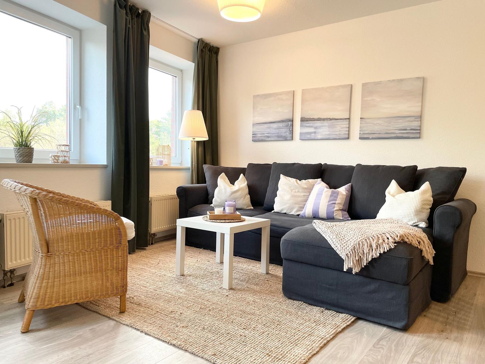Ein Wohnzimmer mit dunklem Sofa, weißen Kissen und einem runden Tisch.