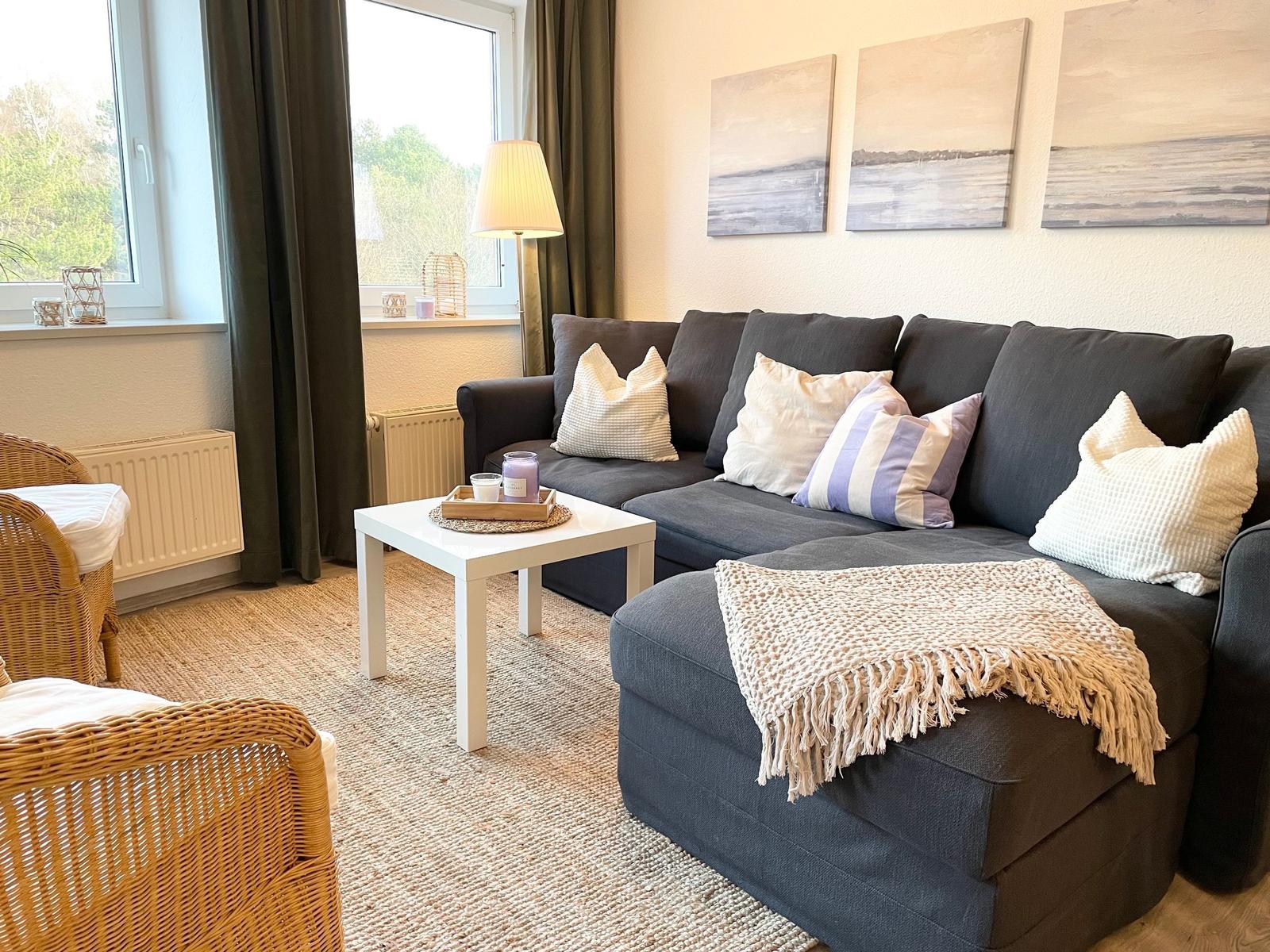Ein Wohnzimmer mit grauem Sofa, weißen Kissen und einem weißen Tisch.