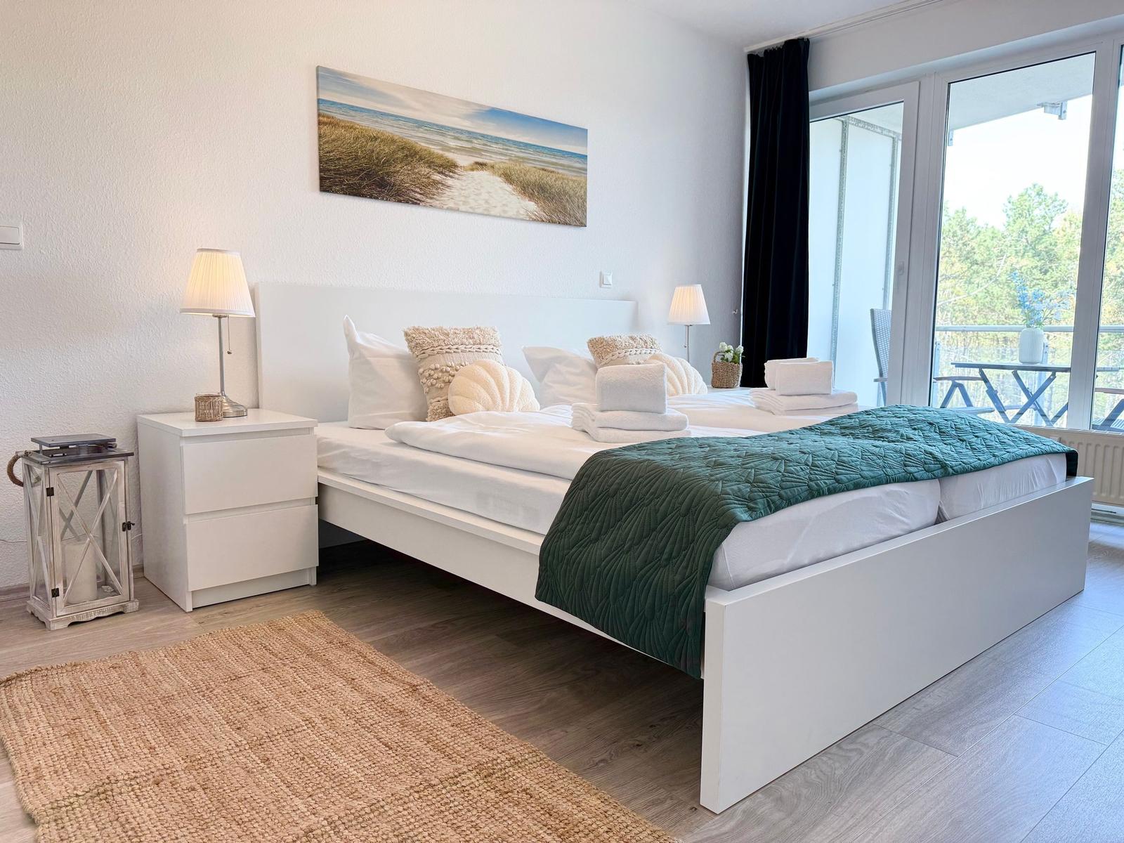 Schlafzimmer mit weißem Bett, grünem Decken und Blick auf Balkon.