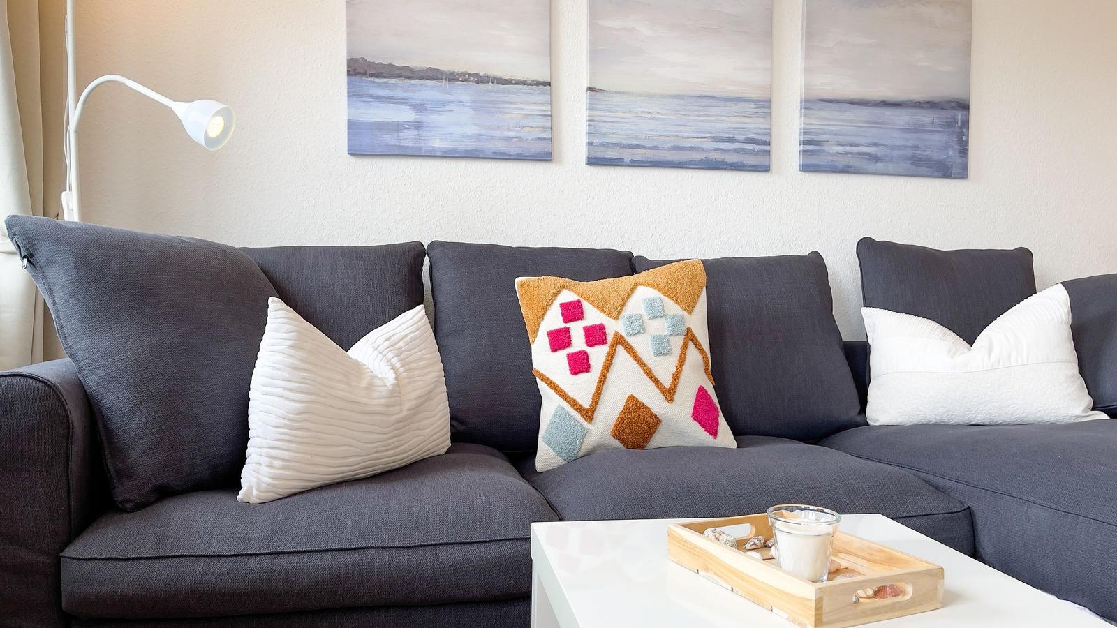 Graße Couch mit Kissen und Wandbildern. Tisch mit Holztablett und Glas.