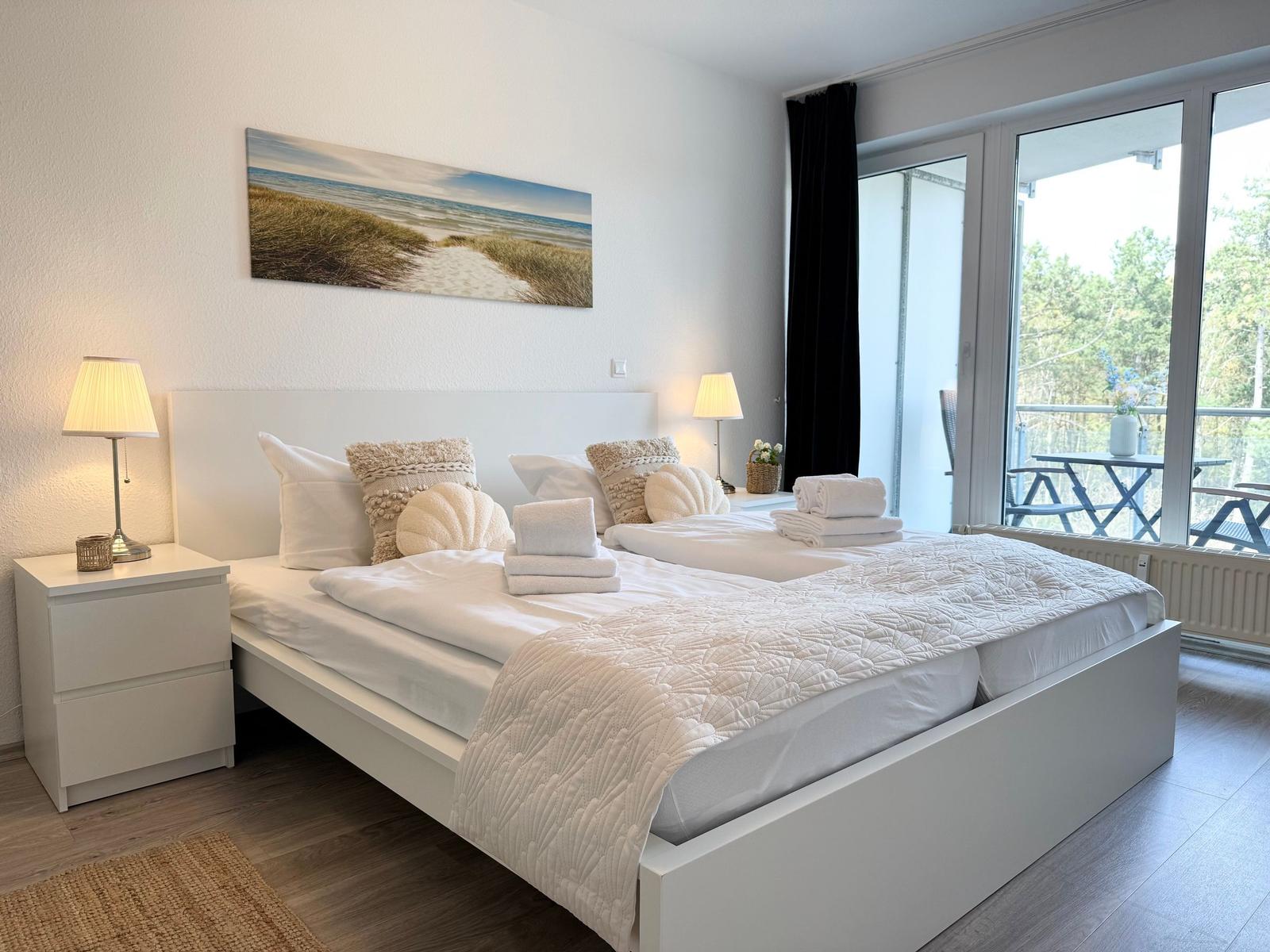 Schlafzimmer mit Doppelbett, zwei Nachttischen und Blick auf Balkon.