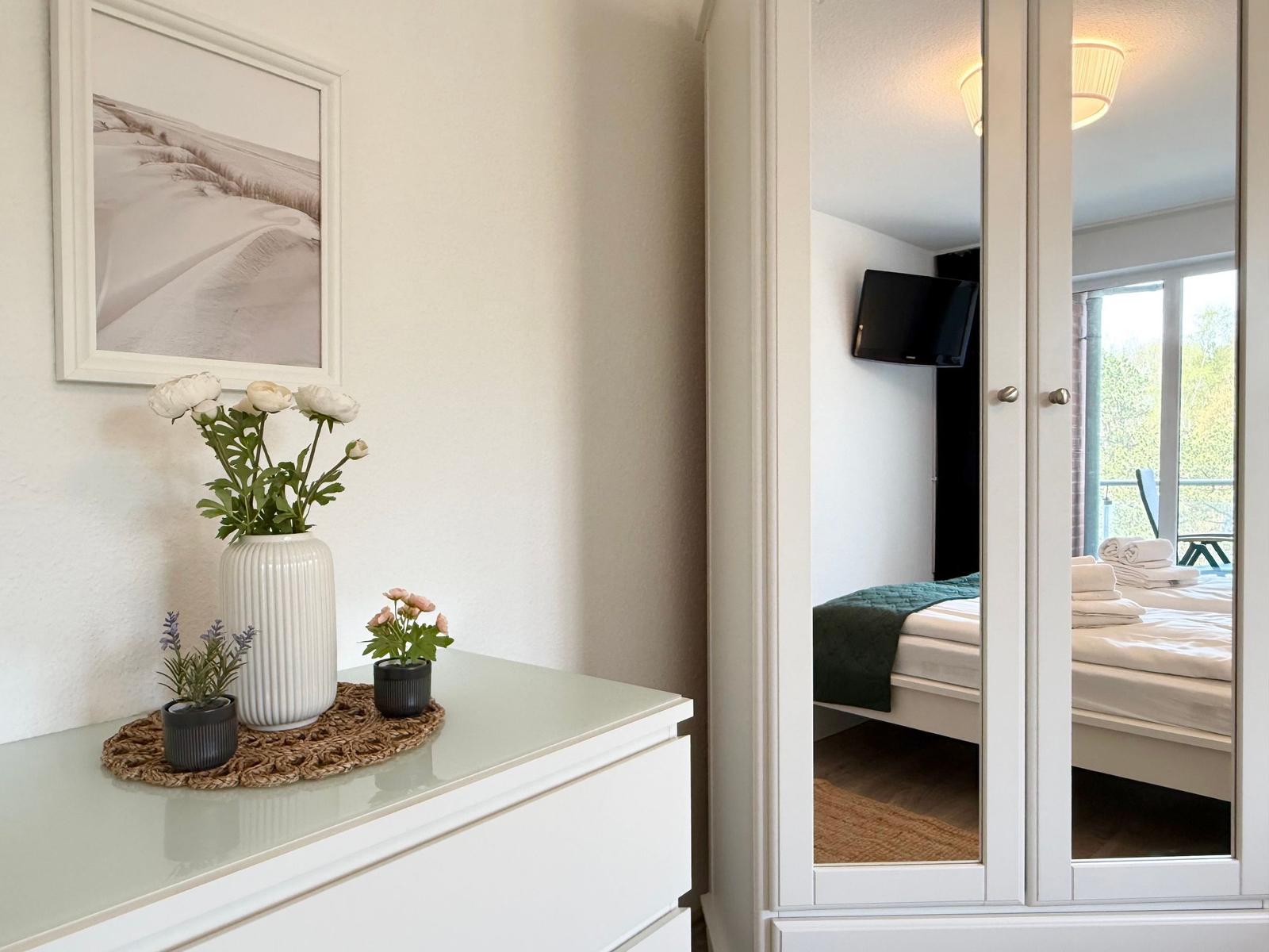 Schlafzimmer mit Spiegelschrank, Bett und TV. Schmucktisch mit Blumen.