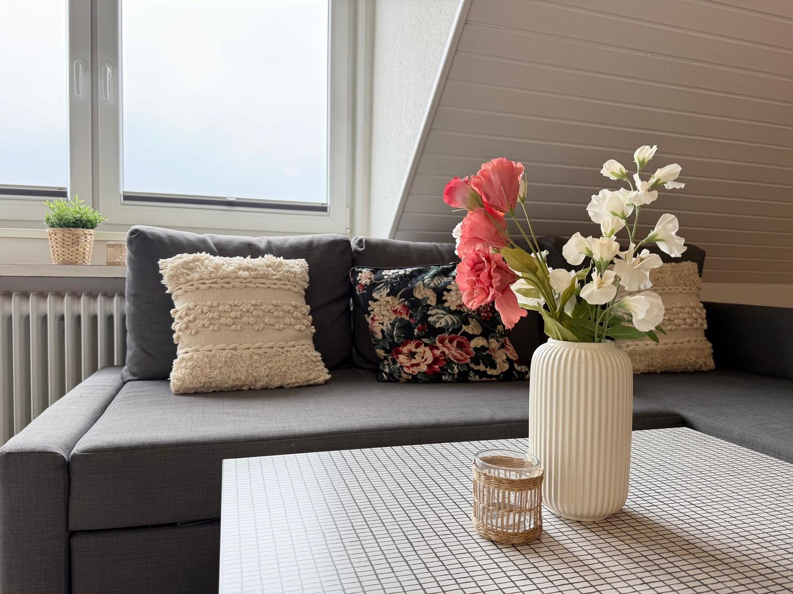 Graße Couch mit Kissen und Blumen auf Tisch vor Fenster