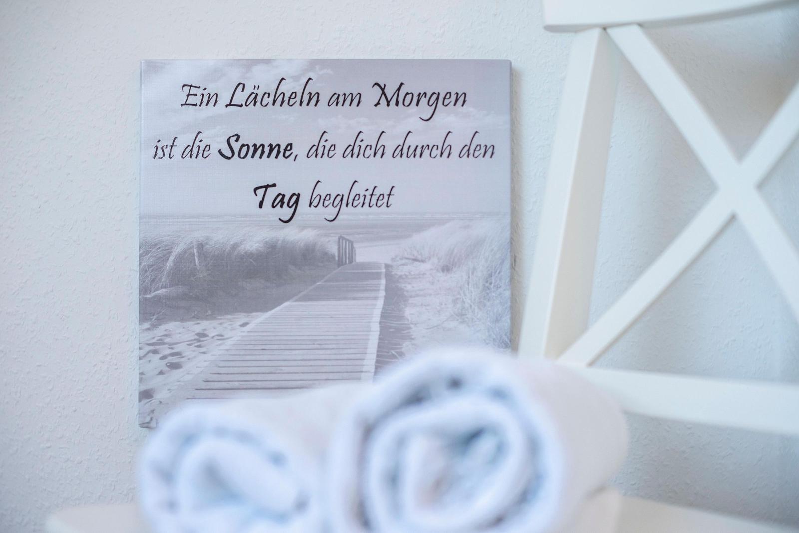 Wandbild mit Strandmotiv und deutscher Inschrift, vorne liegen gefaltete Handtücher.