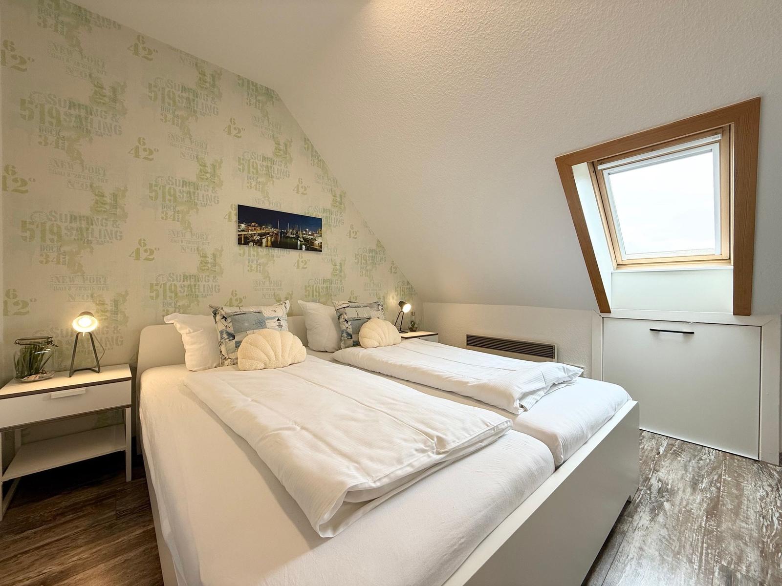 Schlafzimmer mit Doppelbett, Dachschräge, Fenster und Wand mit Aufdruck.