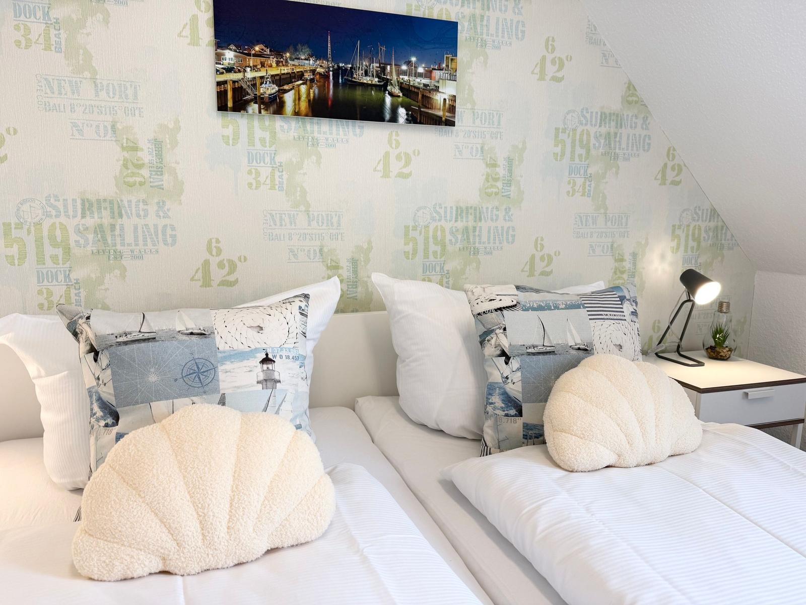 Zwei Betten mit Kissen und Wandbild in einem Schlafzimmer mit gestreiftem Tapete.