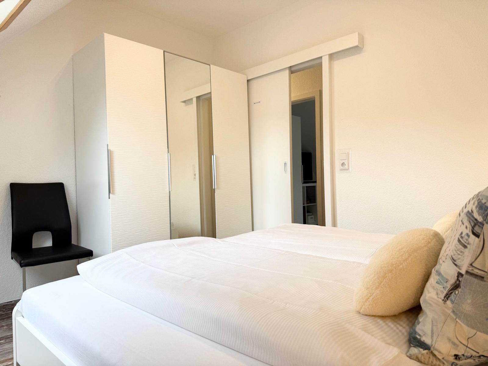 Schlafzimmer mit Bett, Kleiderschrank und Stuhl