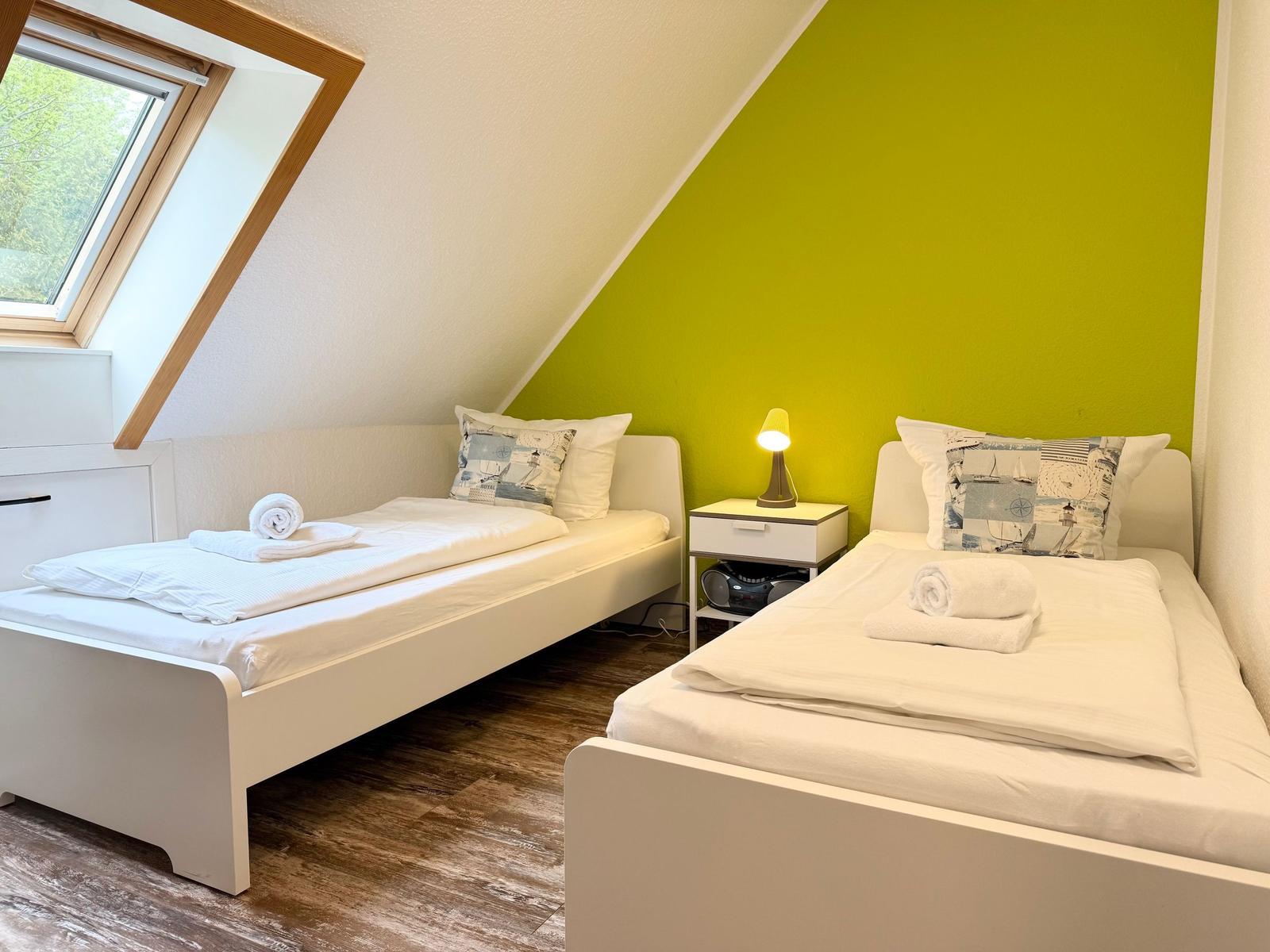 Zwei Einzelbetten in einem Dachzimmer mit grüner Wand und Dachfenster.