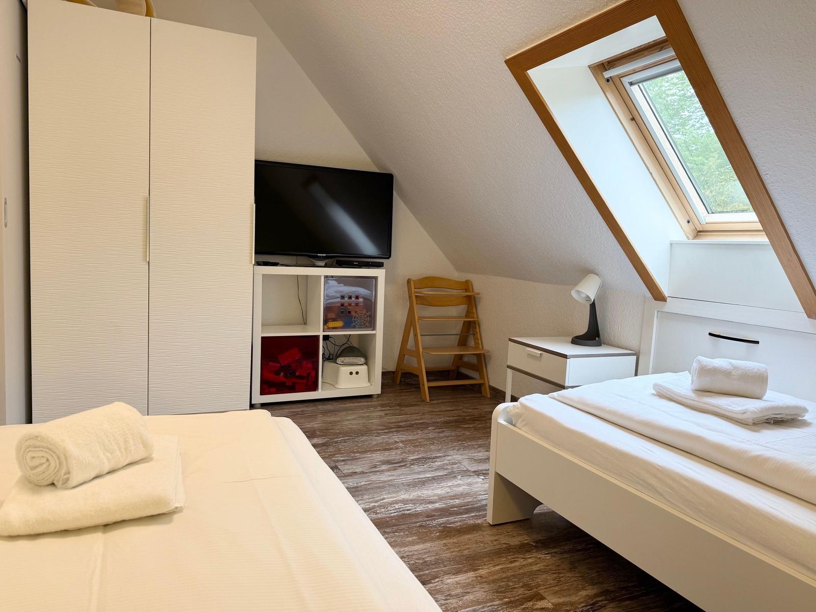 Zimmer mit zwei Betten, Dachfenster und TV. Holzfußboden und weißer Schrank.