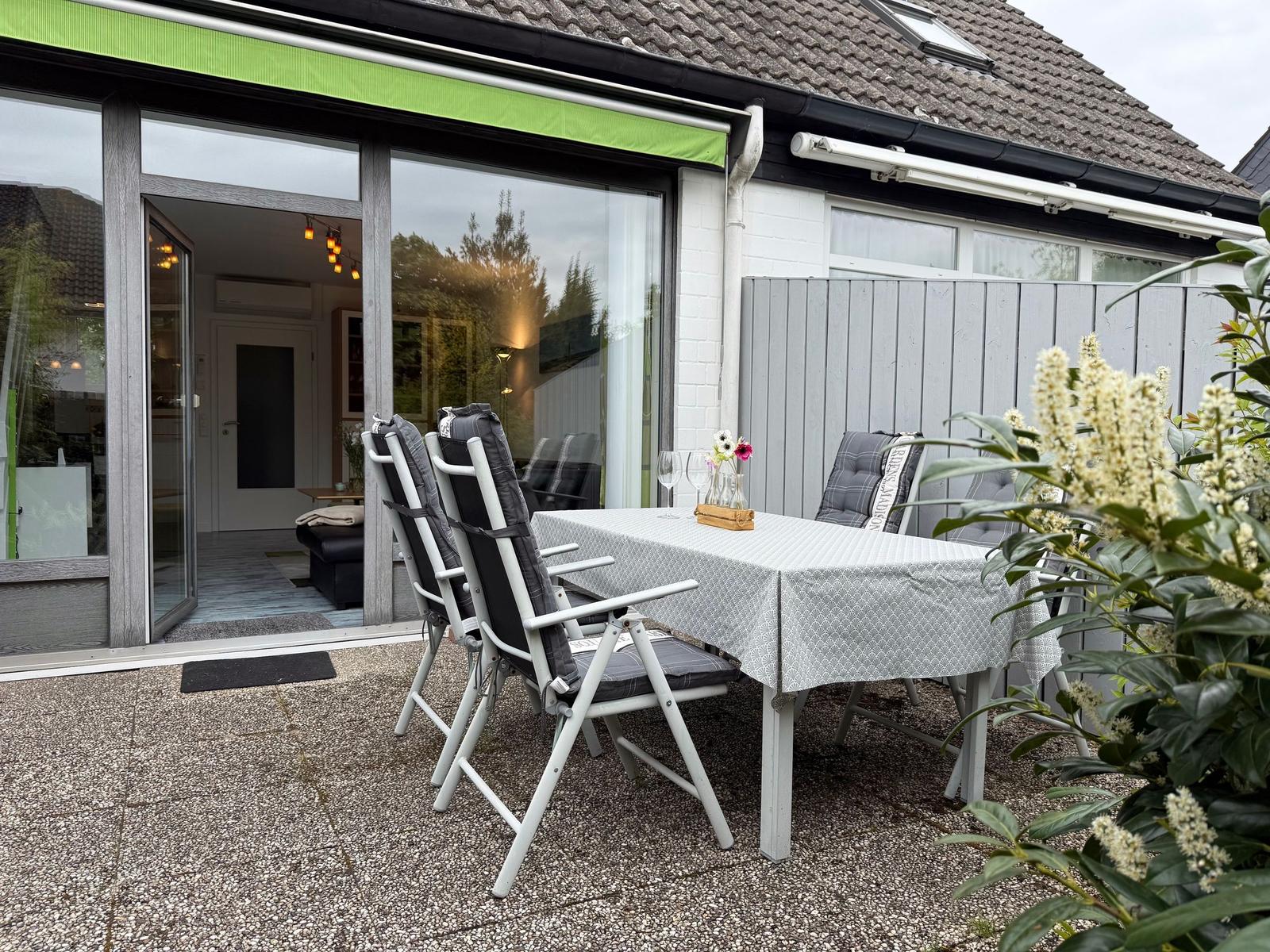 Terrasse mit Tisch und Stühlen, grüne Markise, Blick ins Haus.