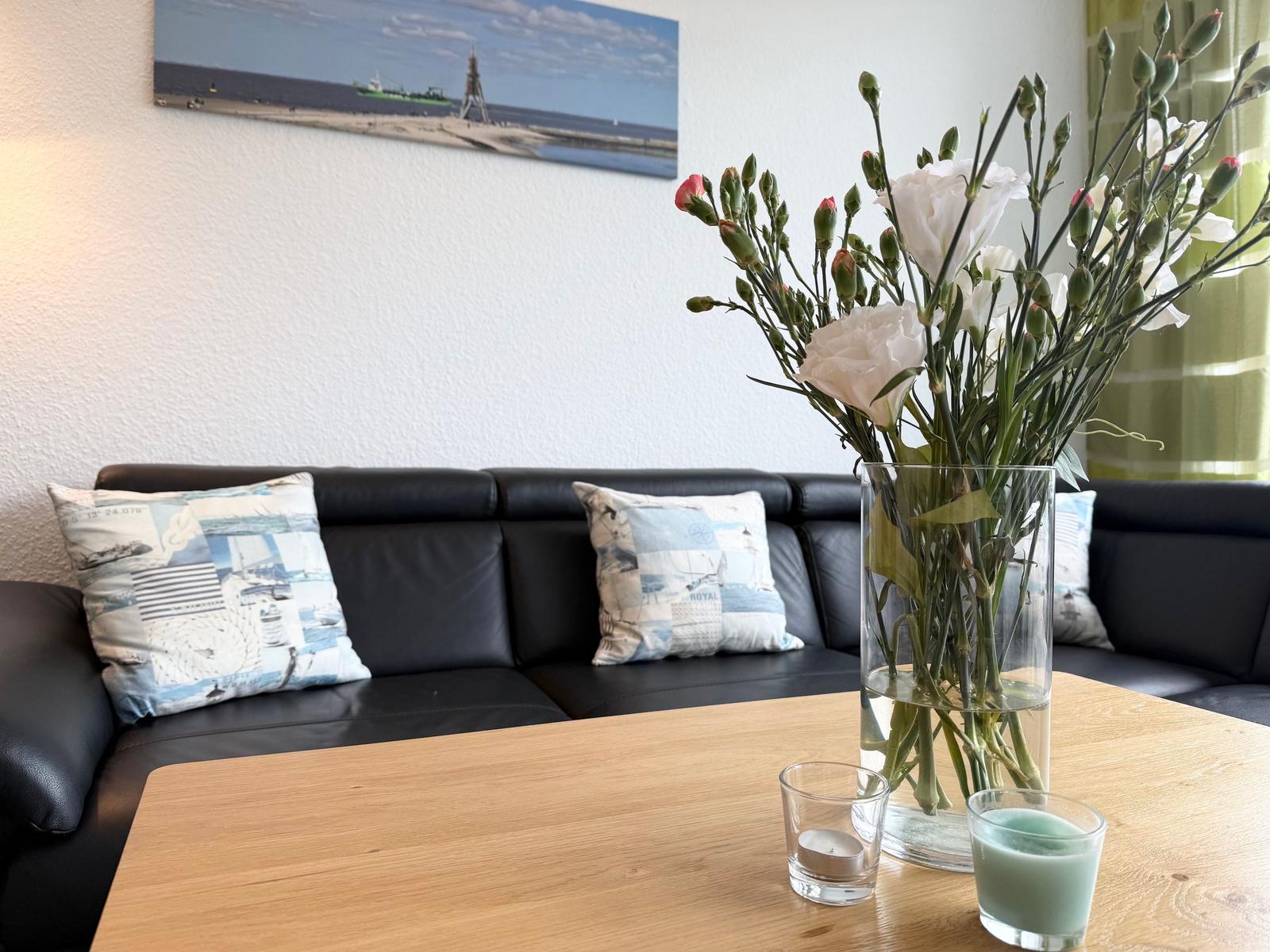 Schwarzes Sofa mit Kissen, Holztisch, Blumenvase und Wandbild an der Wand.