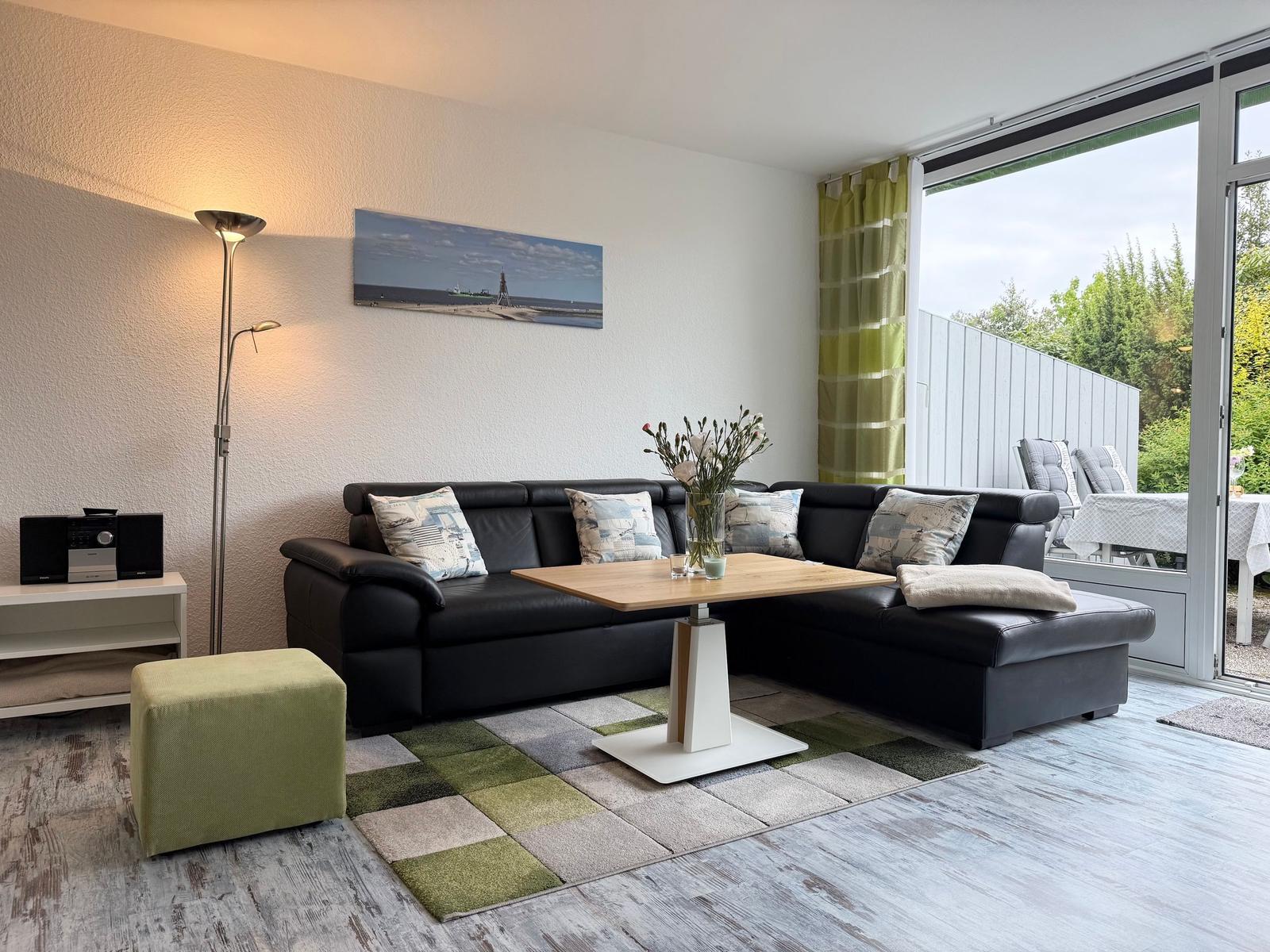 Wohnzimmer mit schwarzer Couch, Holztisch und Blick auf die Terrasse.