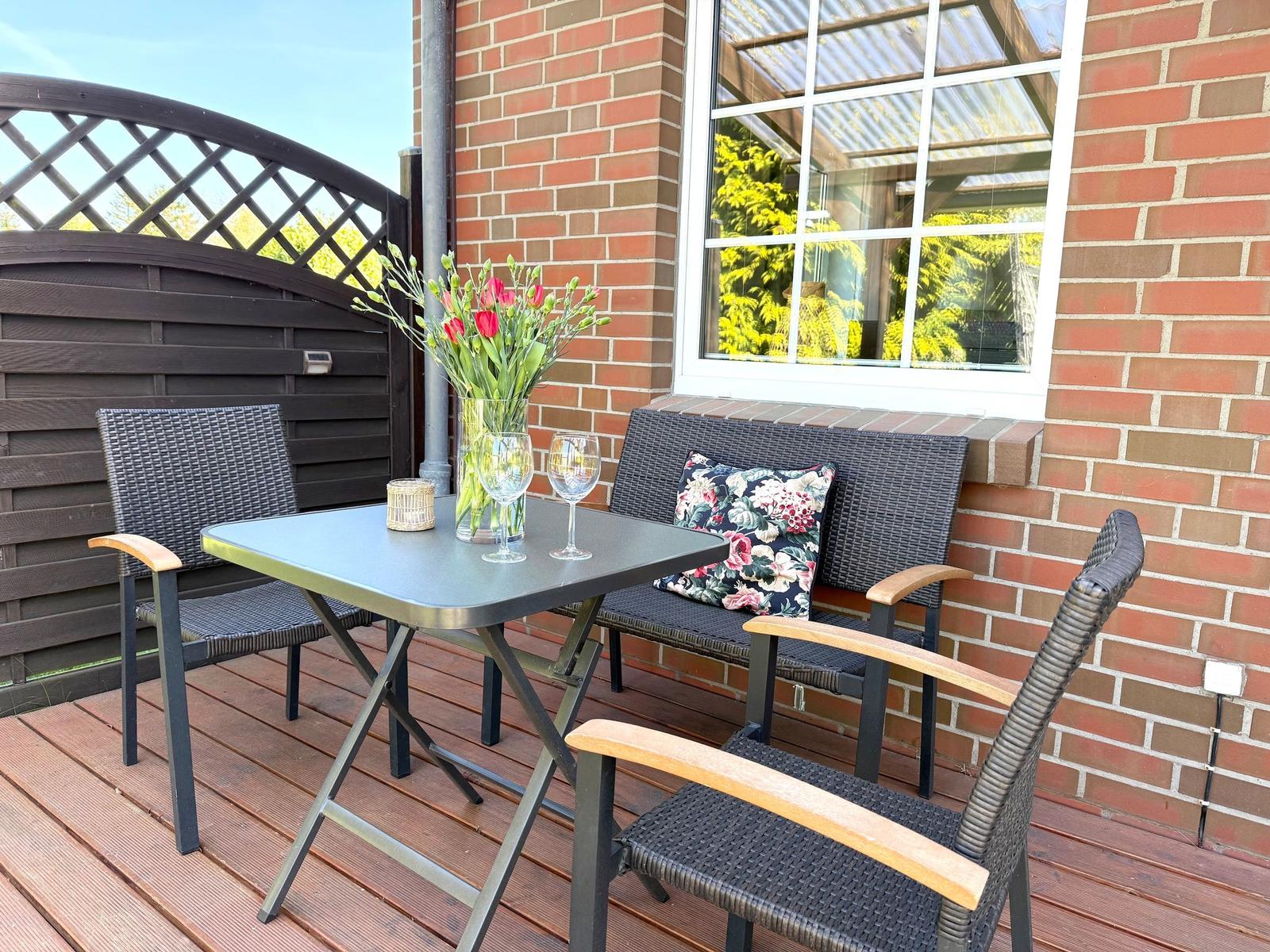 Terrasse mit Tisch, Stühlen und Blumen vor Backsteinmauer.