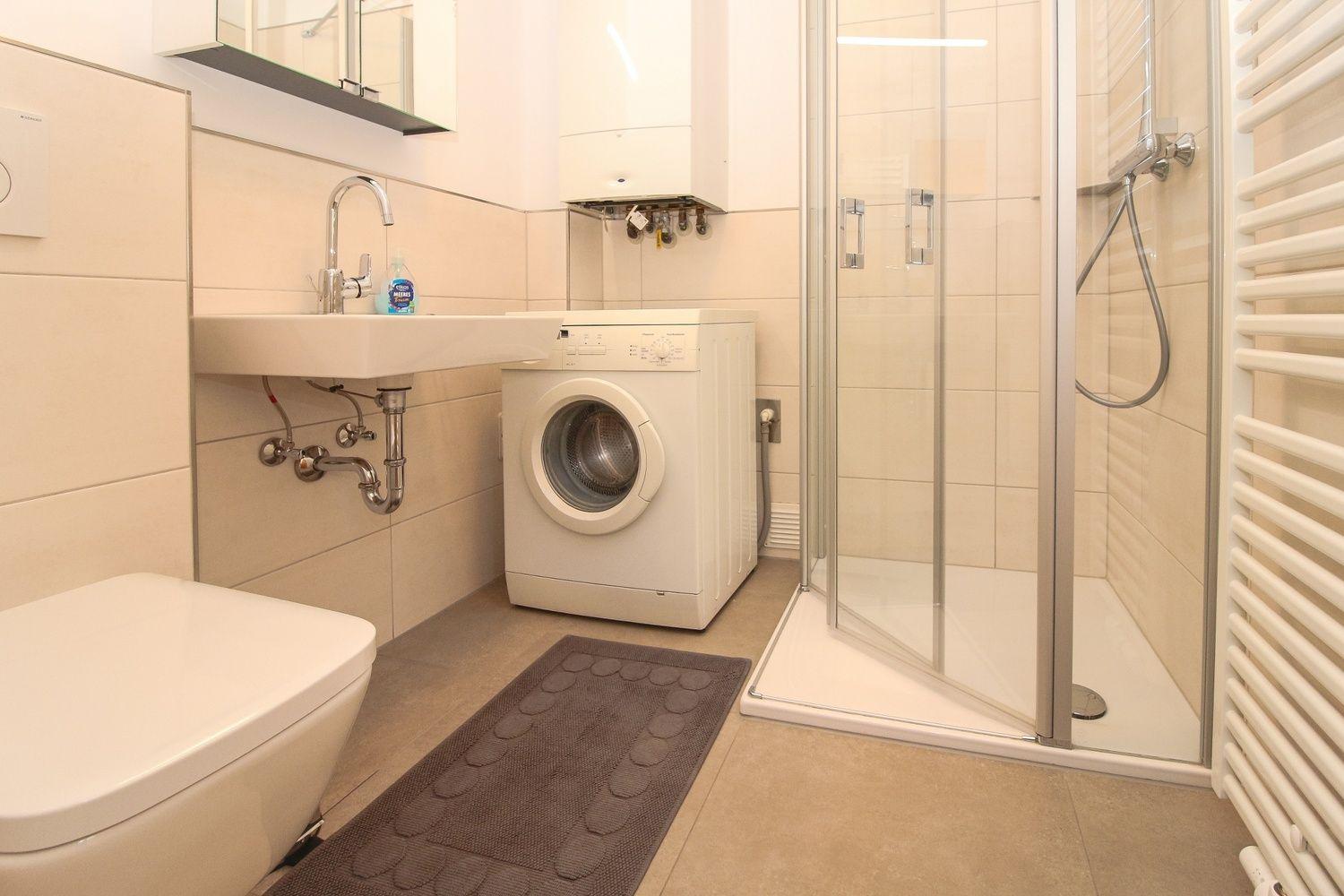 Badezimmer mit Dusche, Waschmaschine und Toilette.