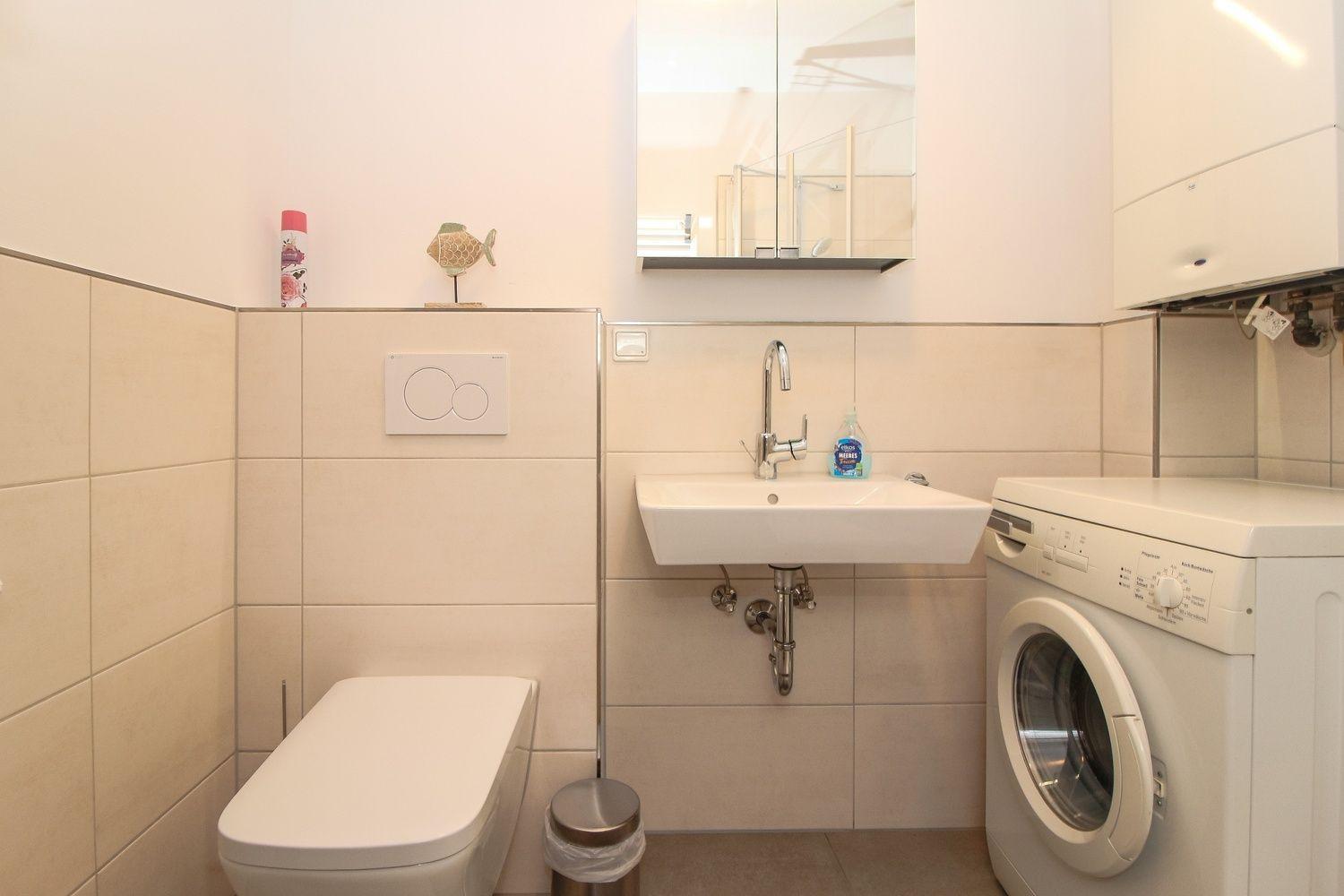 Badezimmer mit Waschmaschine, Spülung und Spiegel.