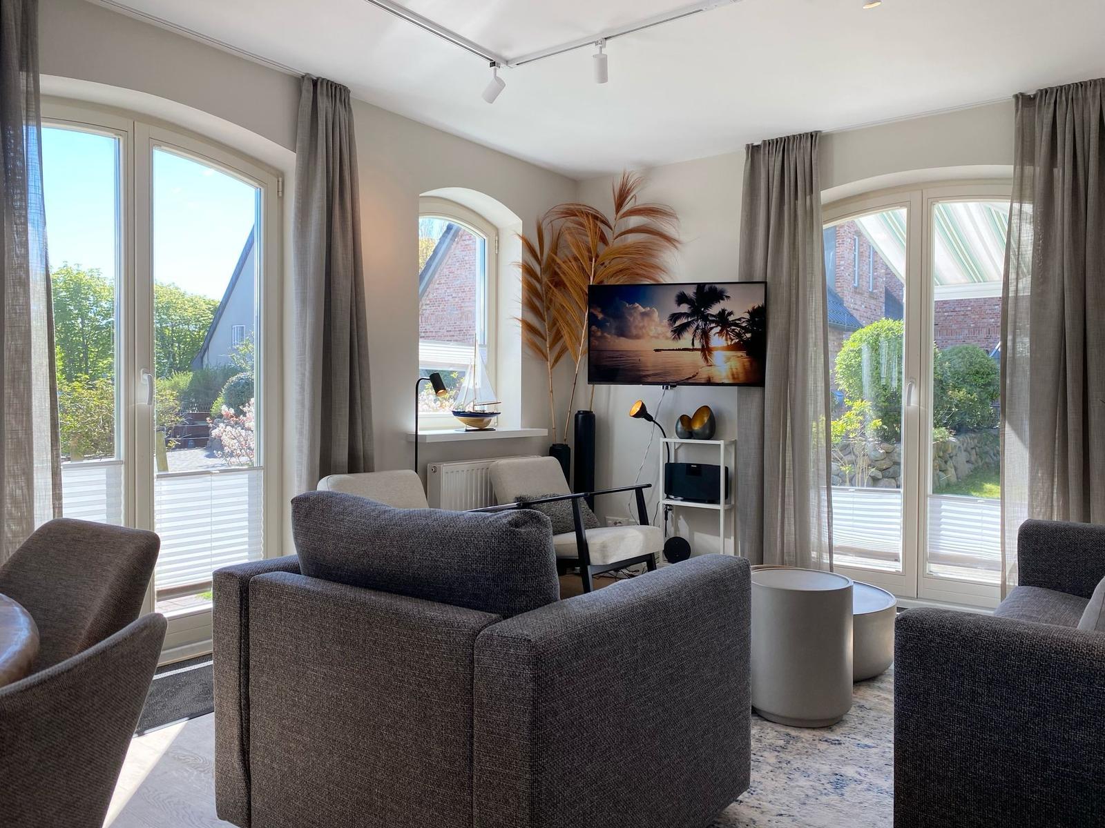 Wohnzimmer mit Sitzgruppe, Fernseher und großen Fenstern zur Aussicht.