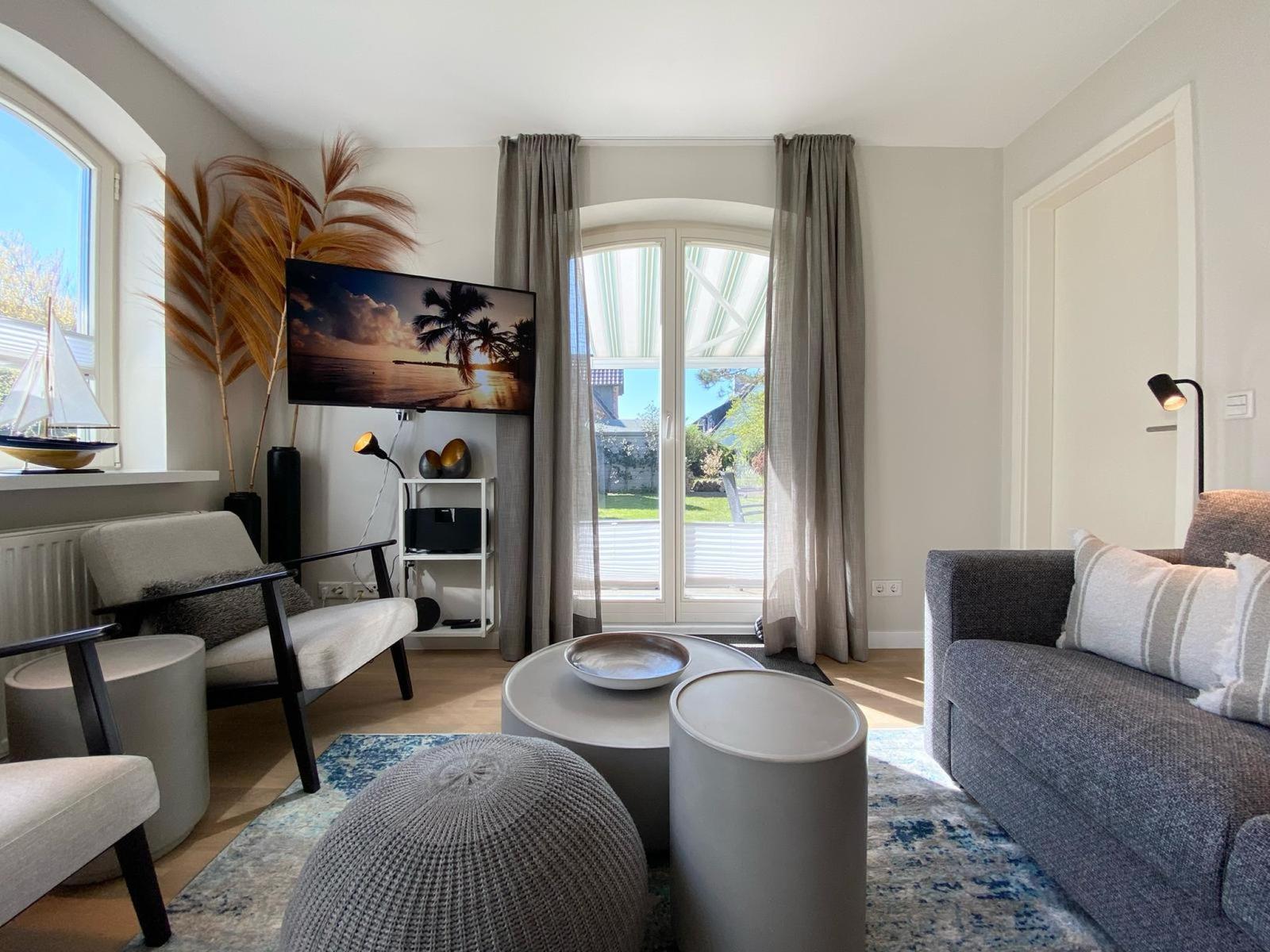 Wohnzimmer mit Sofa, Sessel, Couchtisch und TV. Fenster mit Blick auf Garten.
