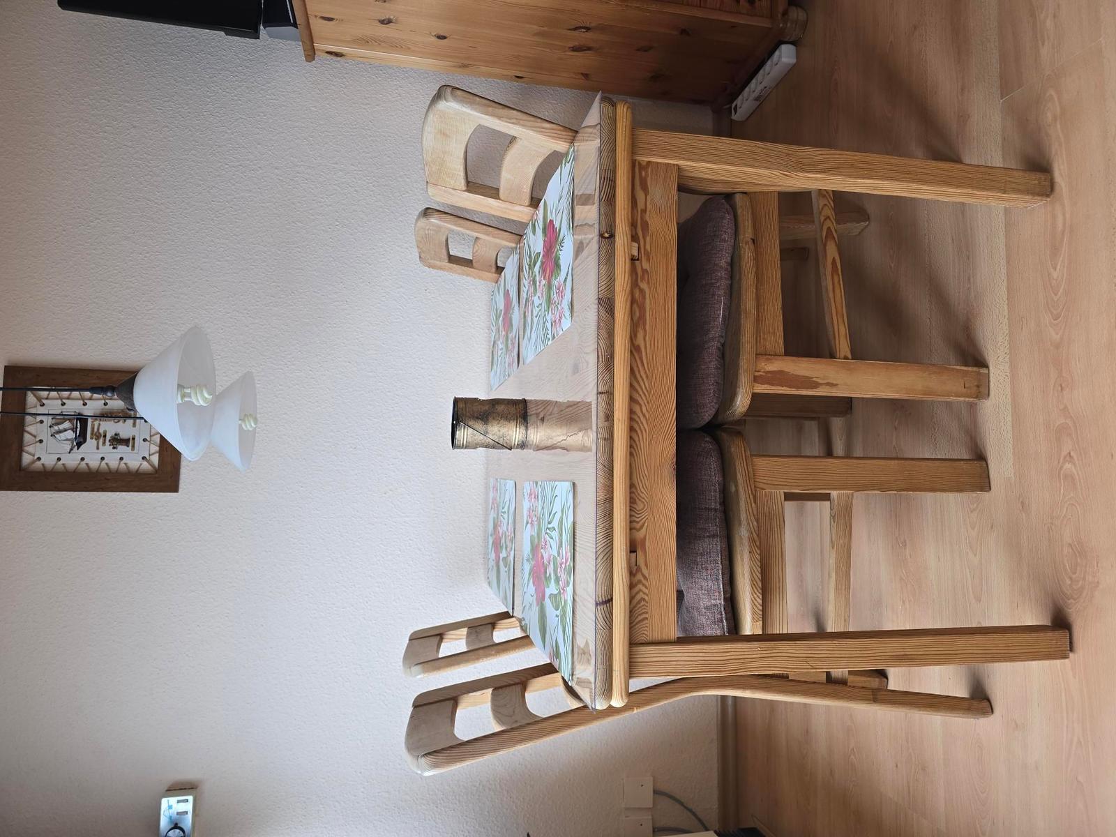 Holztisch mit vier Stühlen und floralen Tischsets.