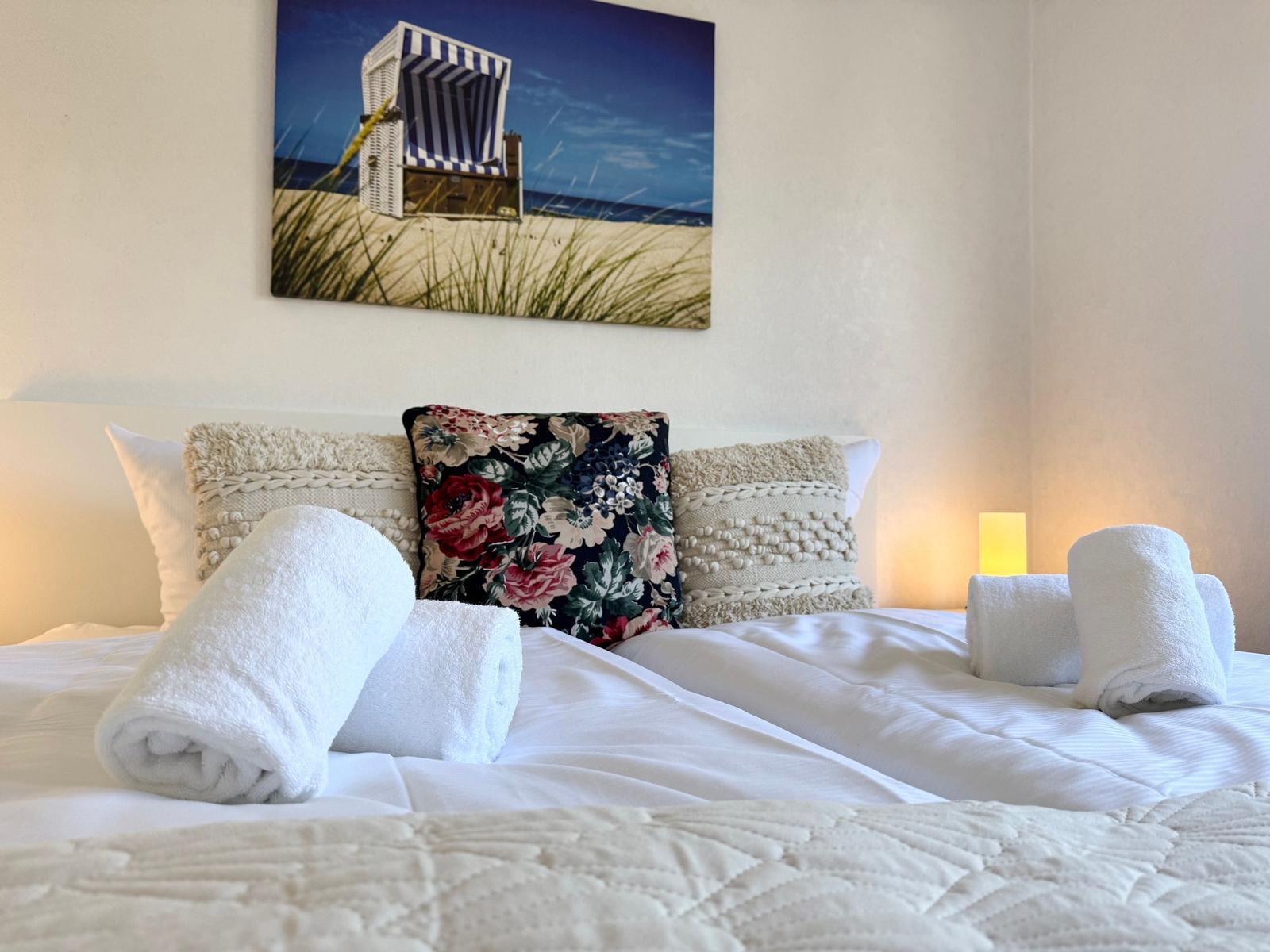 Doppelbett mit Kissen und Handtüchern, Wandbild mit Strandkorb