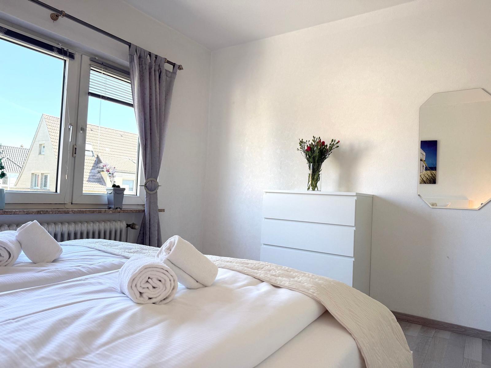 Schlafzimmer mit Bett, Fenster und Schrank. Auf dem Bett liegen Handtücher.