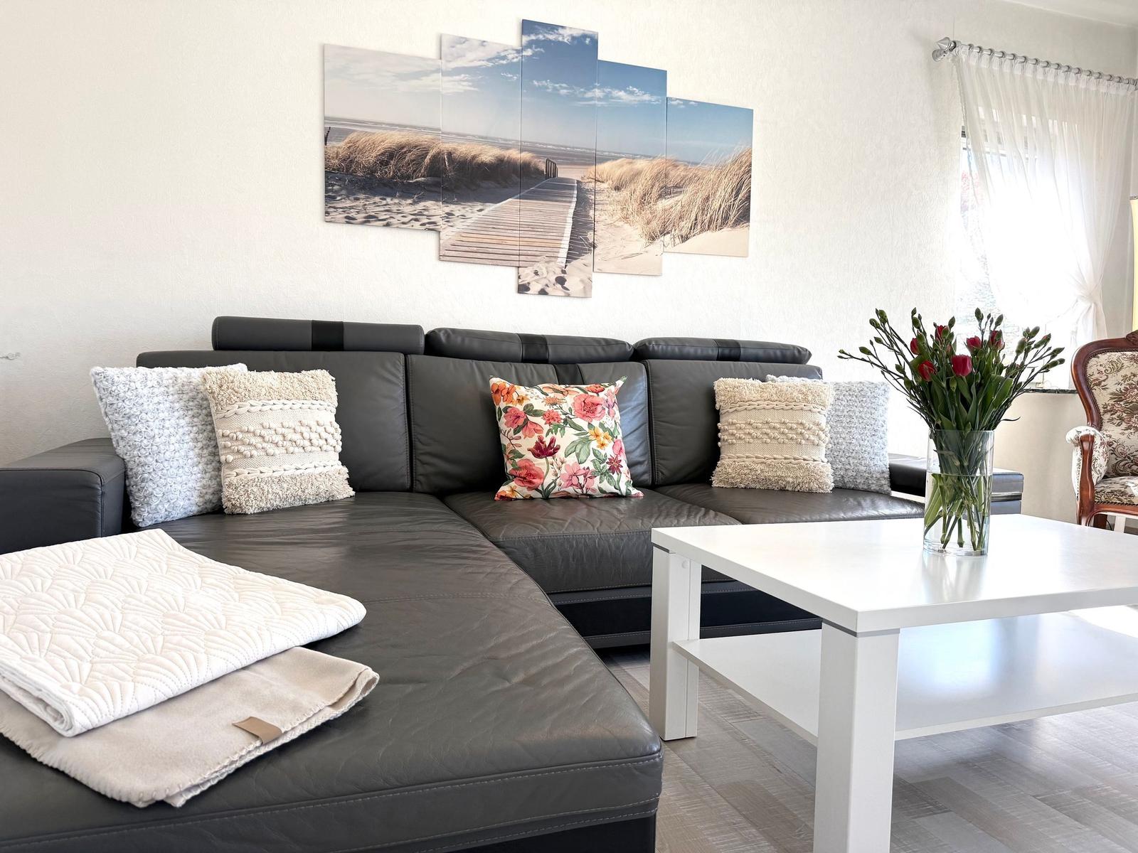 Ein Wohnzimmer mit einem schwarzen Sofa, einem weißen Tisch und einer Wanddekoration.