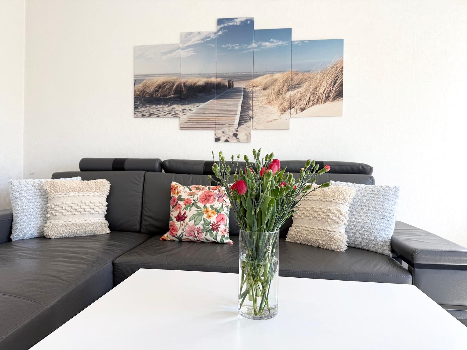Schwarzes Sofa mit Kissen und Blumen auf weißem Tisch vor Wandbild
