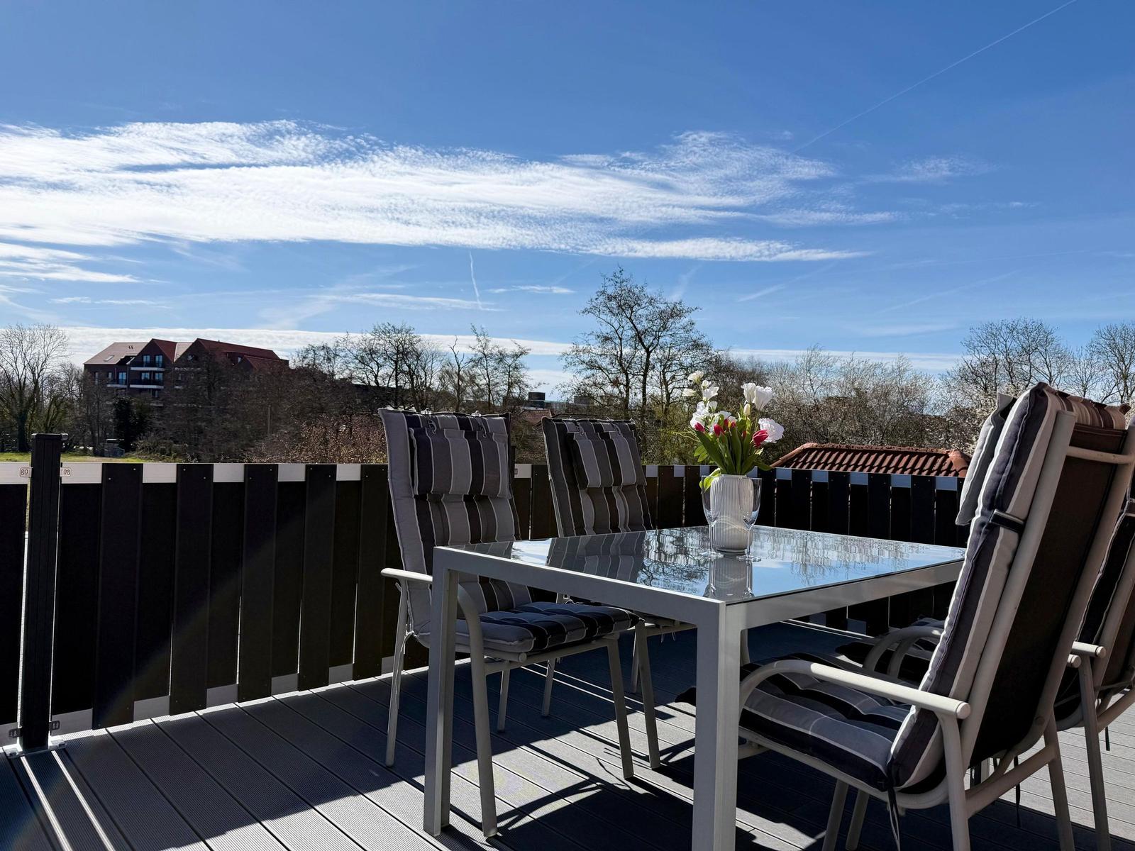 Terrasse mit Tisch und Stühlen, Blick auf Wohngebiet und Himmel.