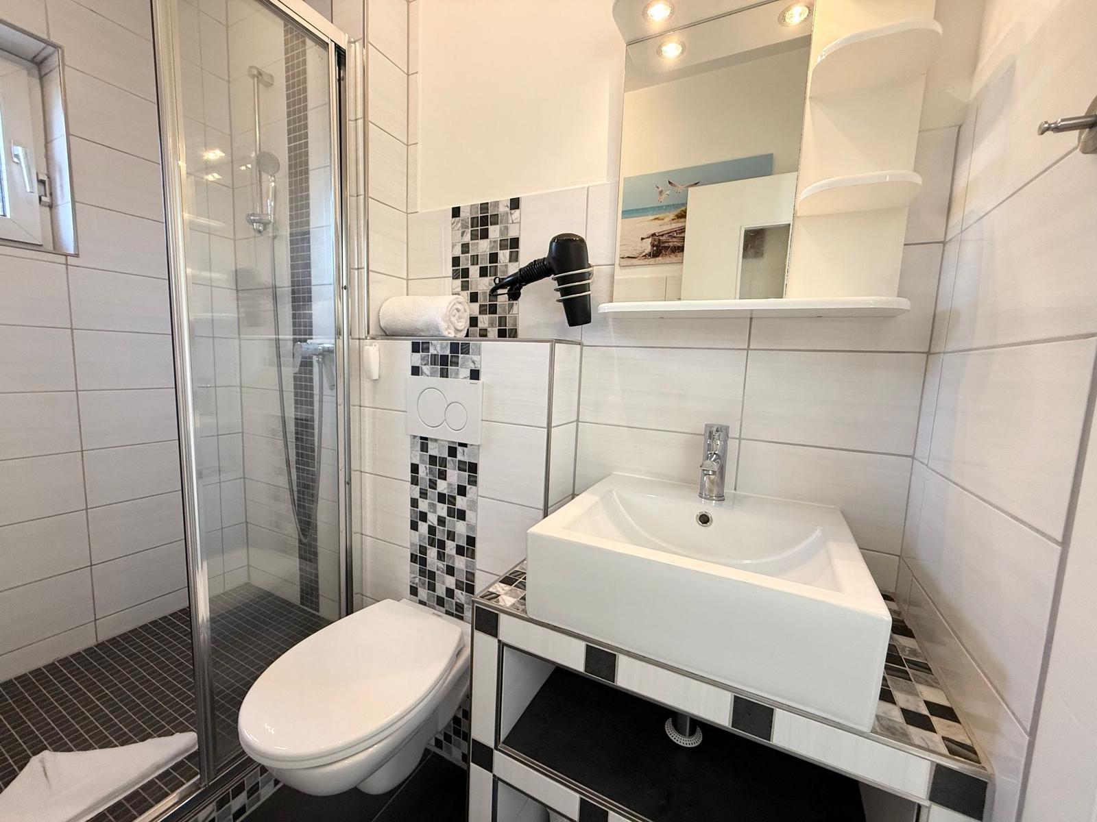 Badezimmer mit Dusche, Waschbecken und Toilette. Fliesen und Spiegel sichtbar.