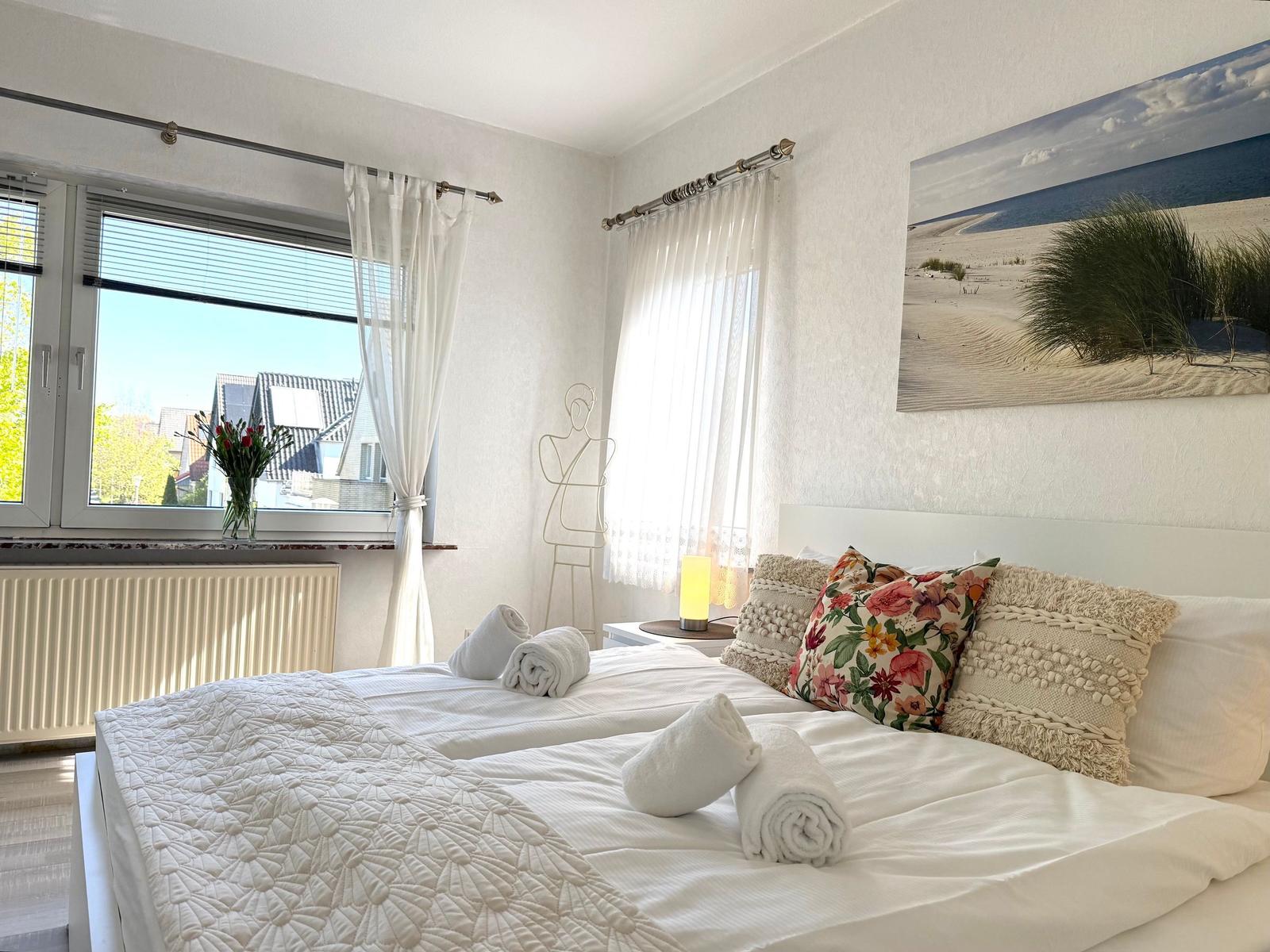 Schlafzimmer mit Doppelbett, Fenster und Wandbild.