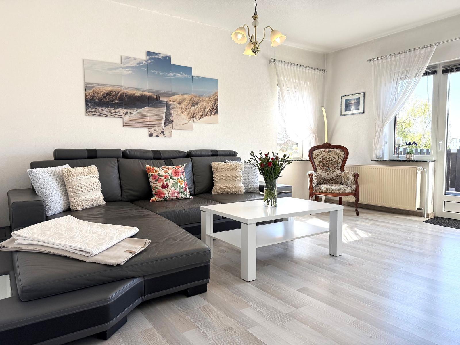 Wohnzimmer mit Sofa, Tisch und Fenster. Wandbild zeigt Strand.