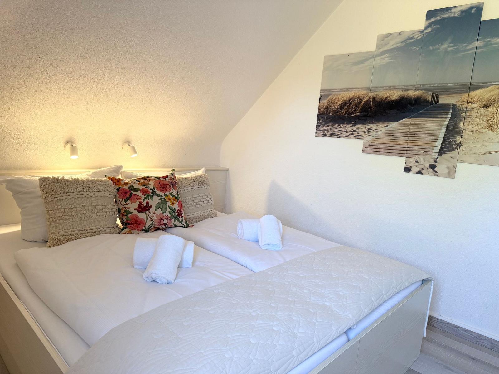 Schlafzimmer mit Doppelbett, dekorativen Kissen und Strandbild an der Wand.