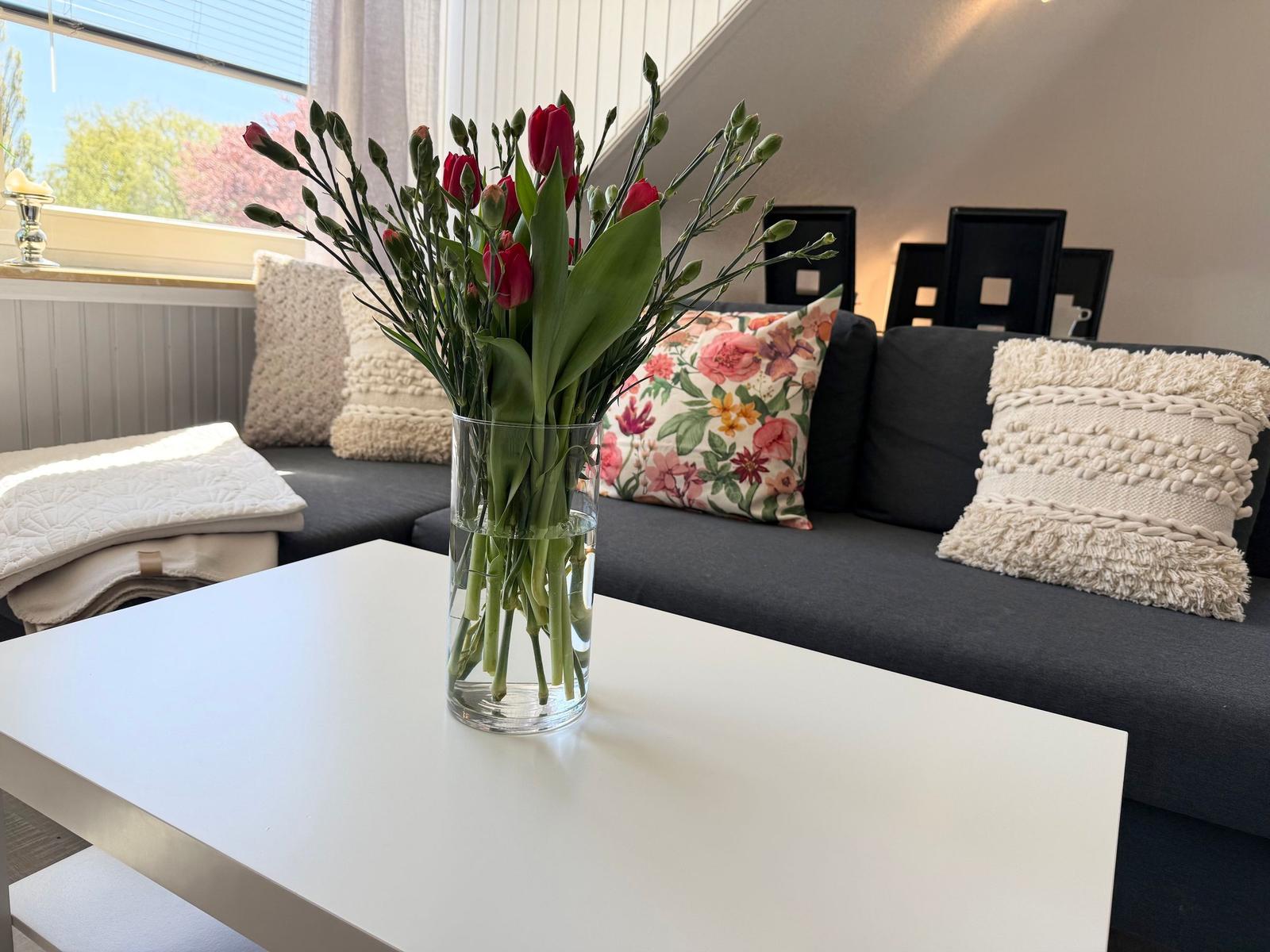 Ein grauer Sofa mit Kissen, ein weißer Tisch und eine Blumenvase.