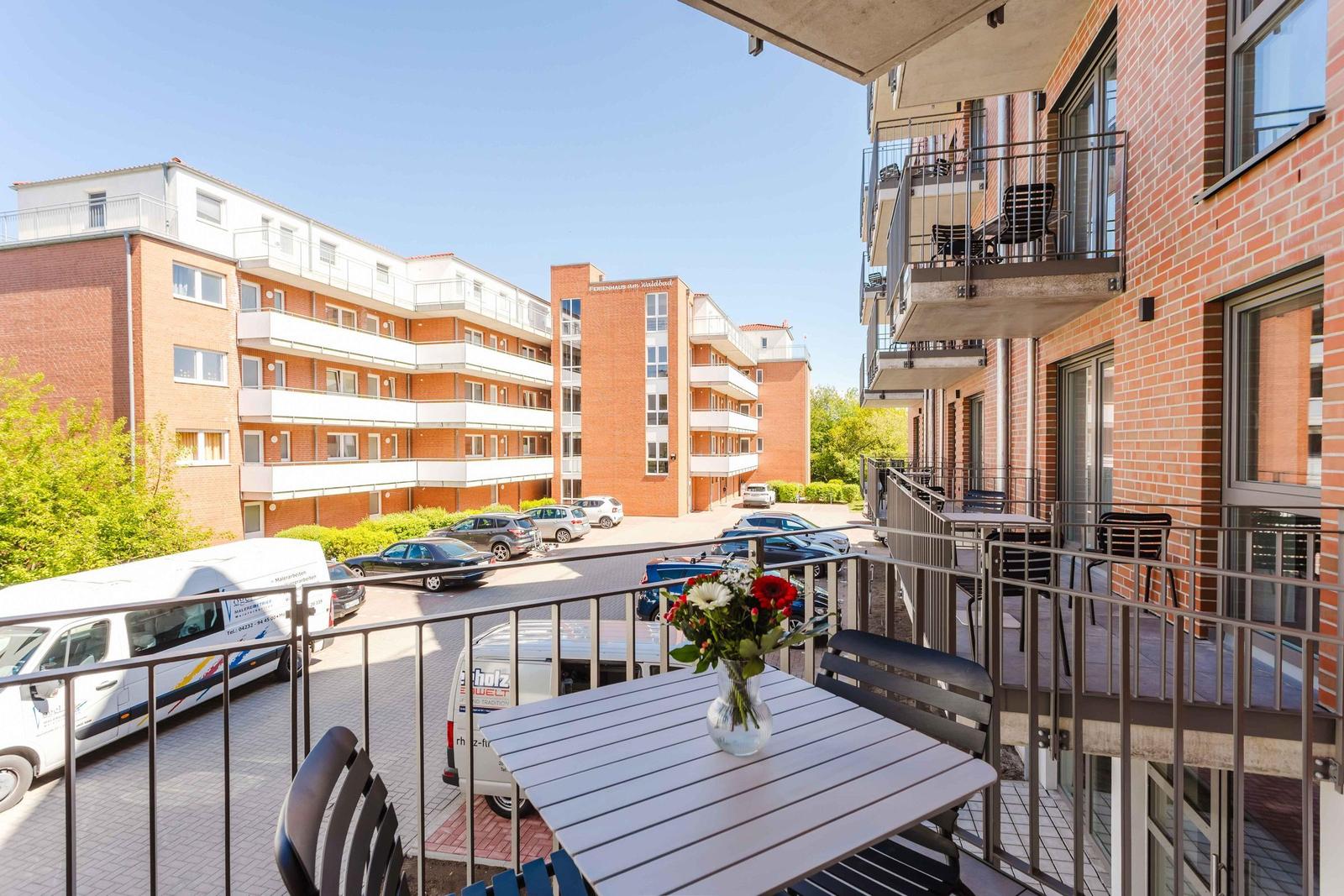Terrasse mit Tisch und Stühlen. Im Hintergrund mehrstöckige Wohnhäuser und Parkplätze.