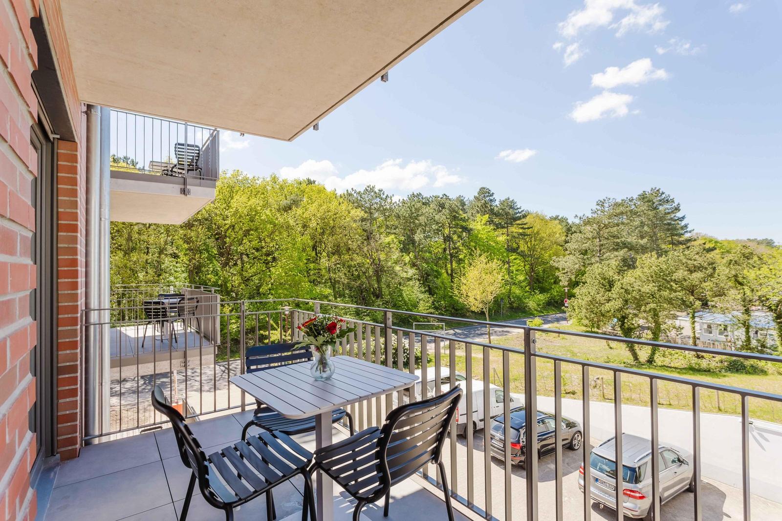 Terrasse mit Tisch und Stühlen, Blick auf grüne Bäume und Parkplatz.